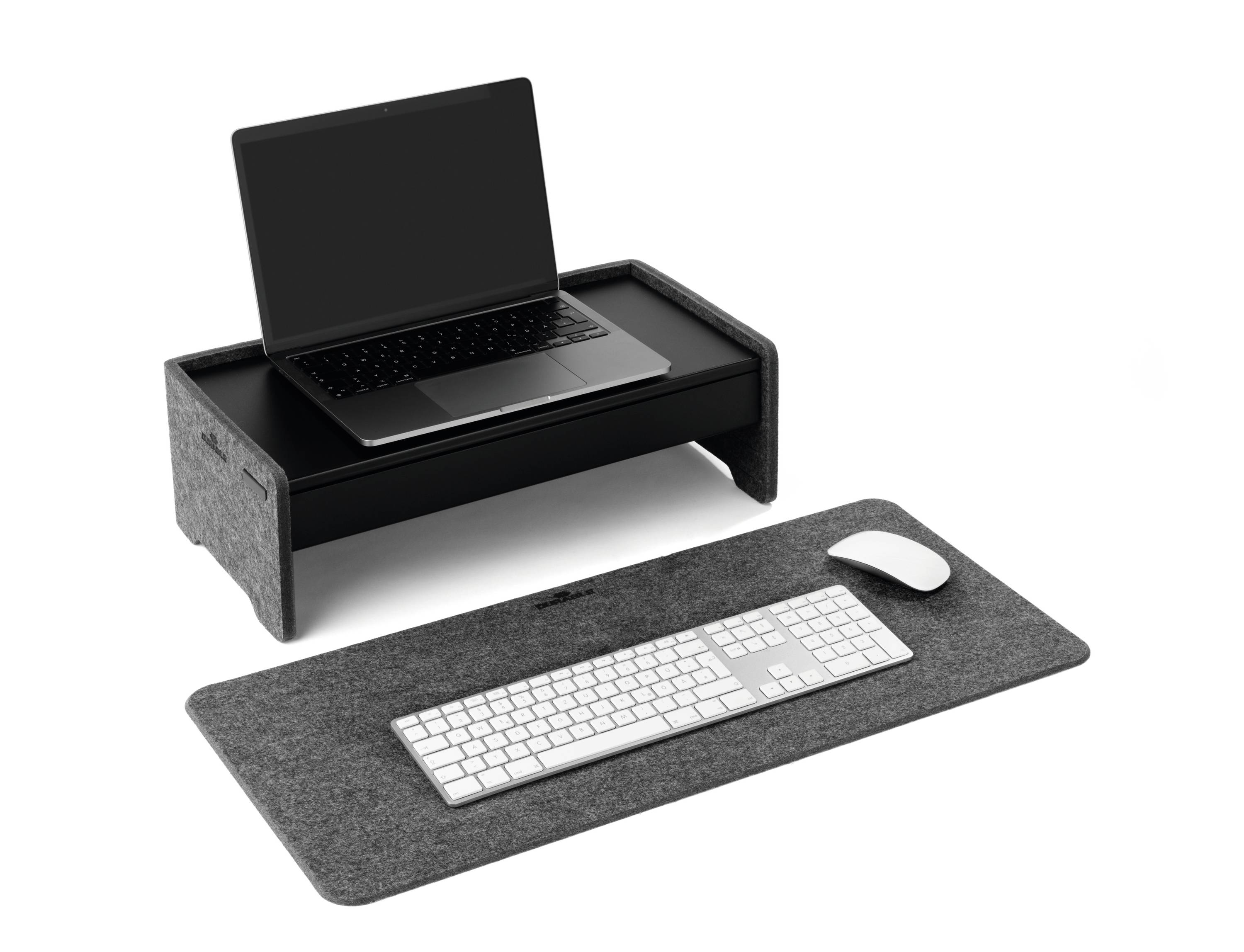 Laptop auf einem erhöhten grauen Ständer, darunter eine Tastatur und Maus auf einer grauen Filzunterlage. Modernes, minimalistisches Design.