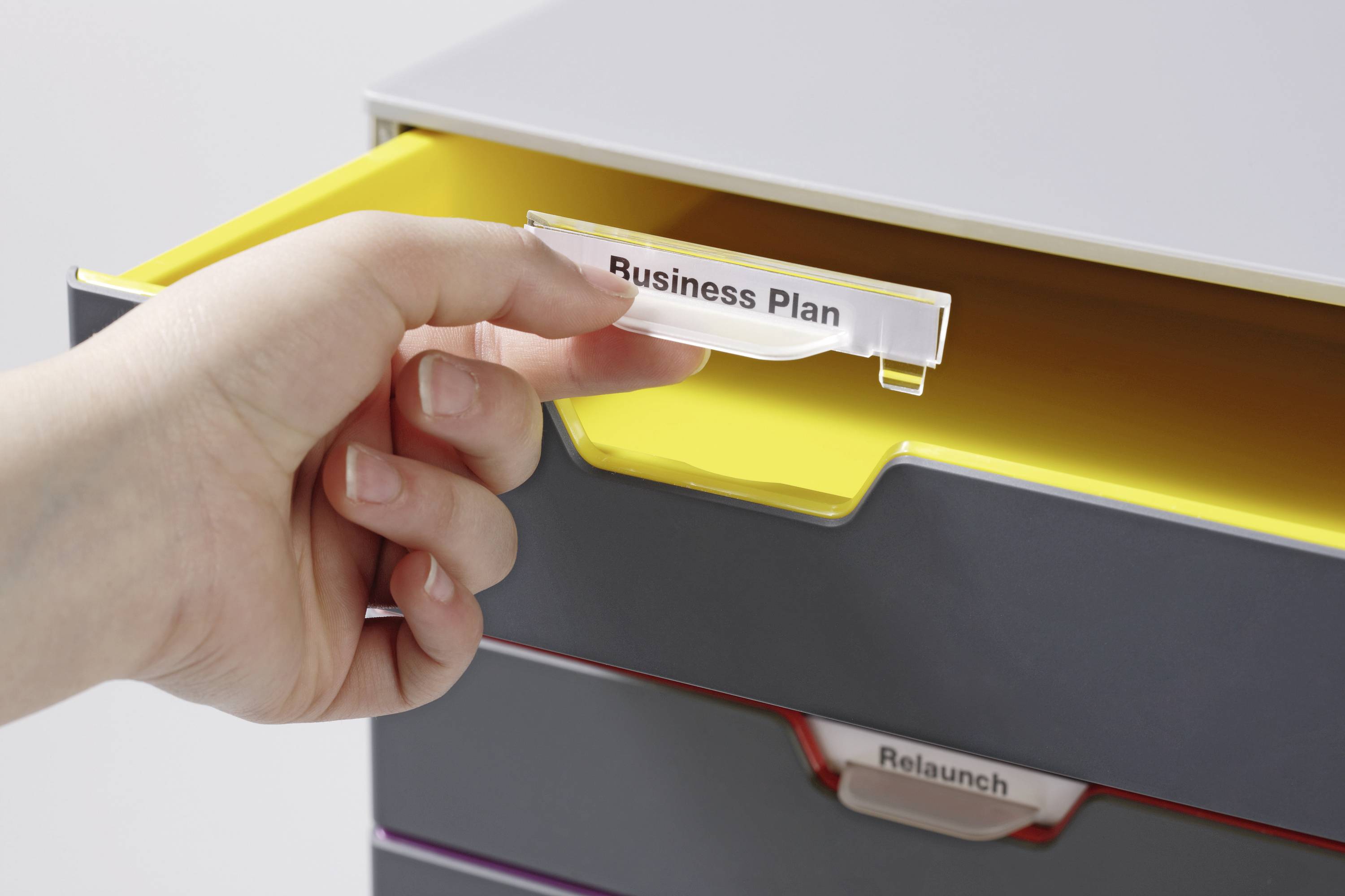 Eine Hand zieht eine Schublade mit dem Etikett 'Business Plan' heraus. Darunter ist eine Schublade mit dem Etikett 'Relaunch' sichtbar.