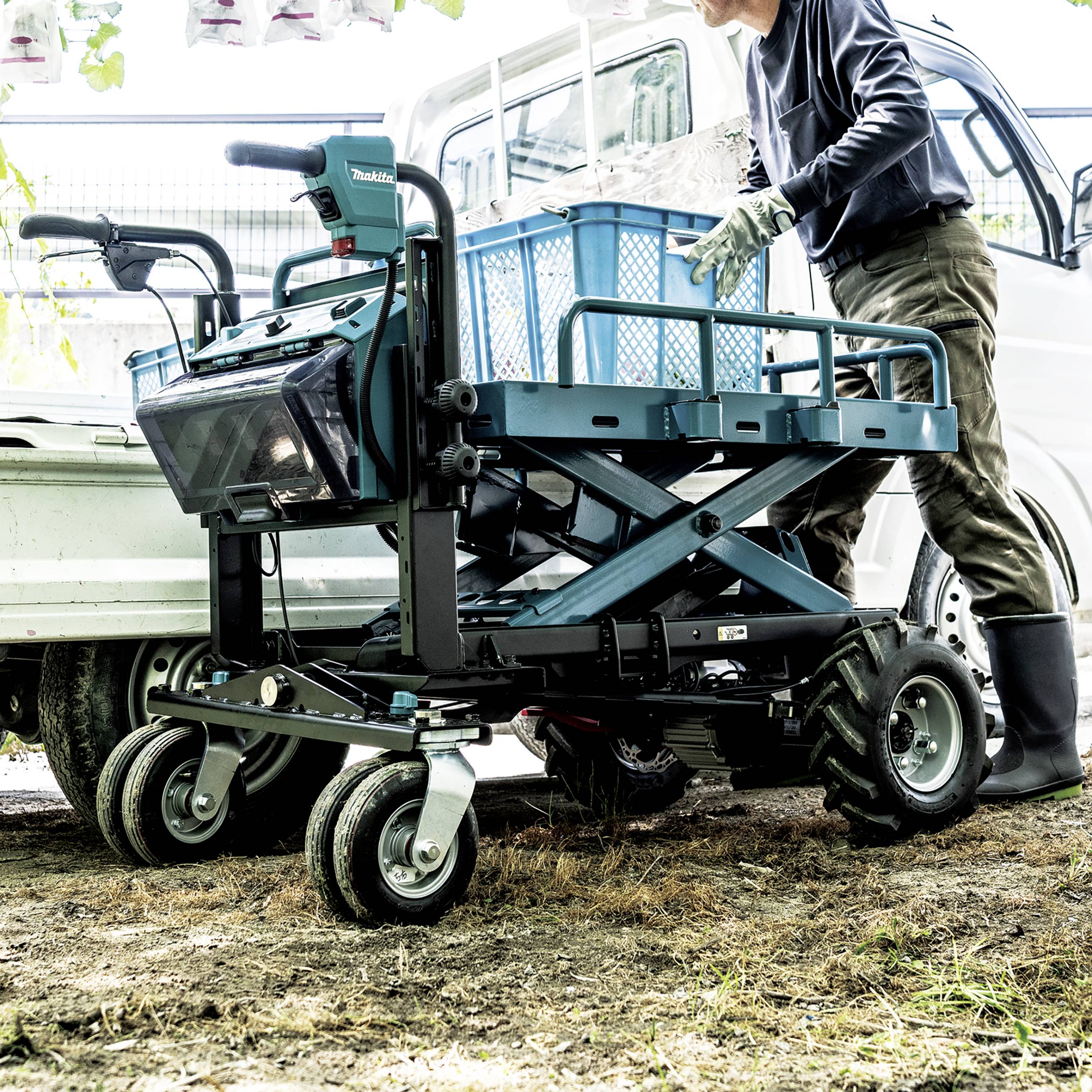 Eine Person belädt einen blauen Lastenwagen mit einem Metallkorb auf klappbaren Rädern. Im Hintergrund ist ein weißes Fahrzeug zu sehen.