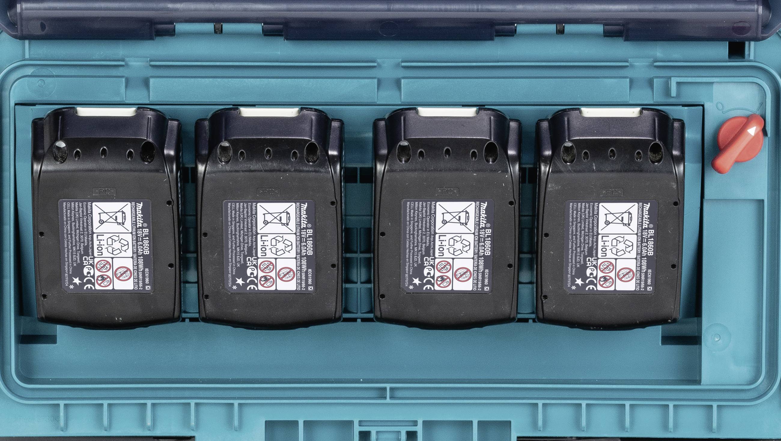 Vier schwarze Akkus liegen nebeneinander in einem blauen Koffer. Warnsymbole auf jedem Akku sind sichtbar.