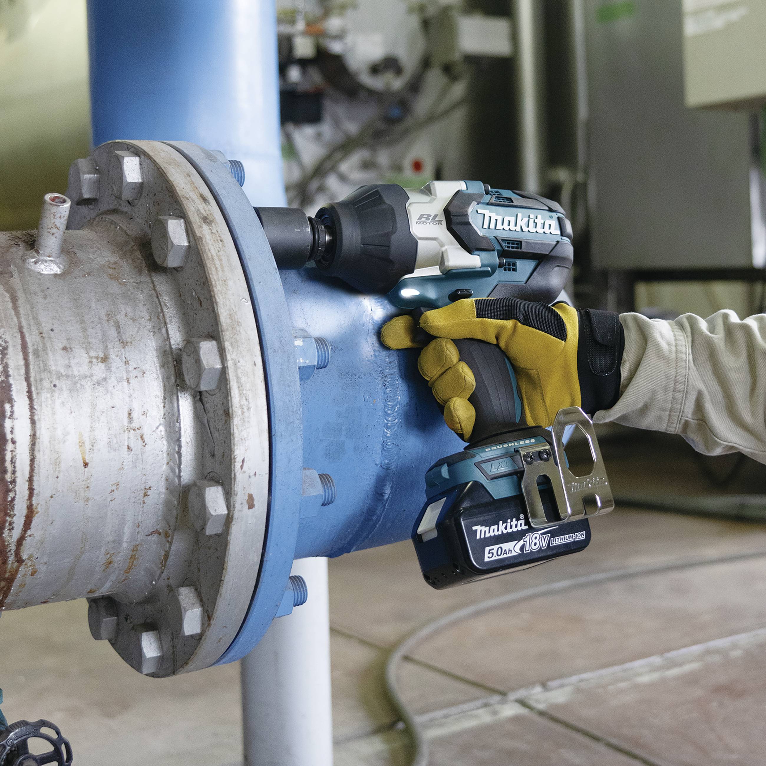Eine Person benutzt einen Makita-Akkuschrauber, um eine große blaue Rohrverbindung in einer industriellen Umgebung zu befestigen.