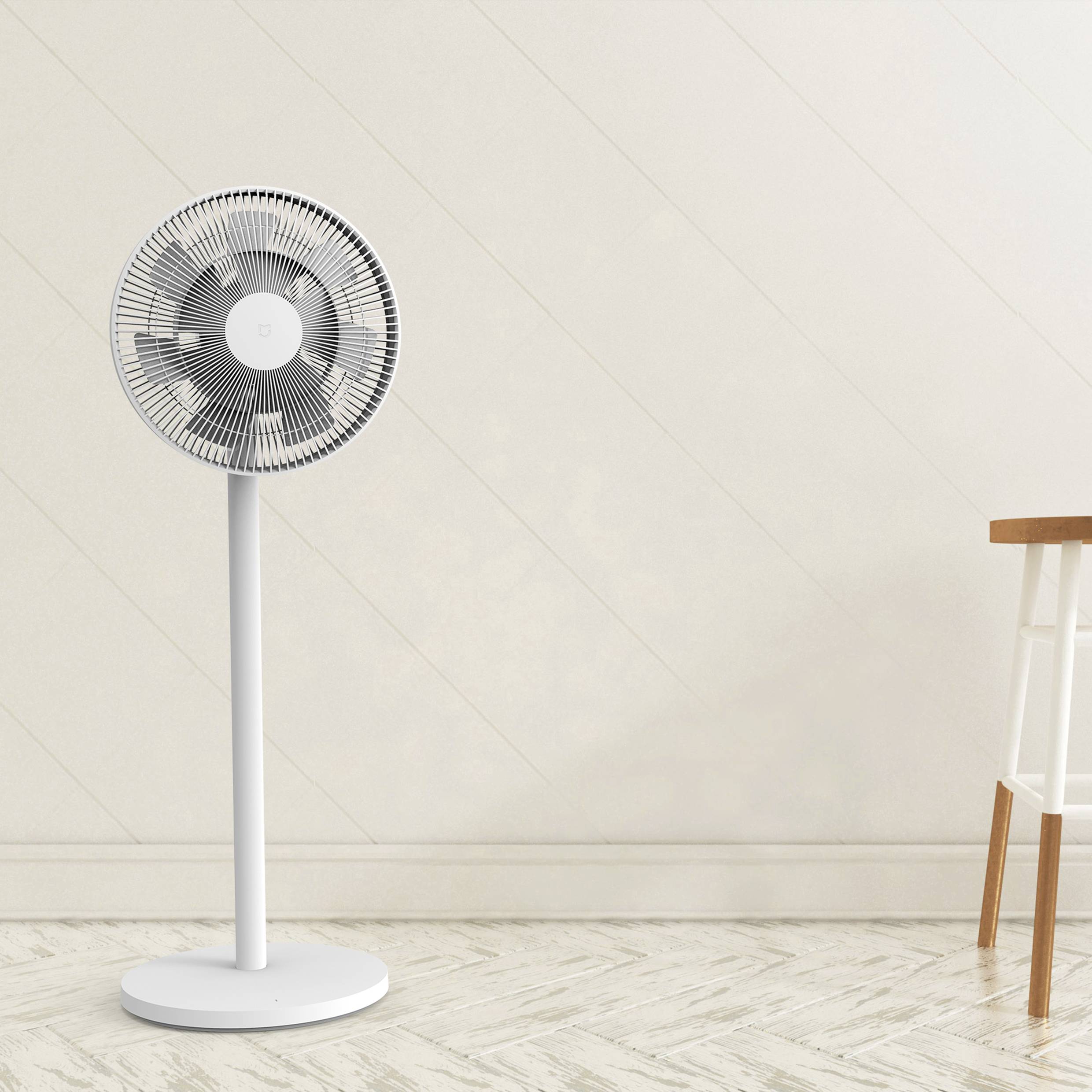 Ein weißer Standventilator steht in einem Raum mit Holzboden. Daneben befindet sich ein kleiner Holztisch.