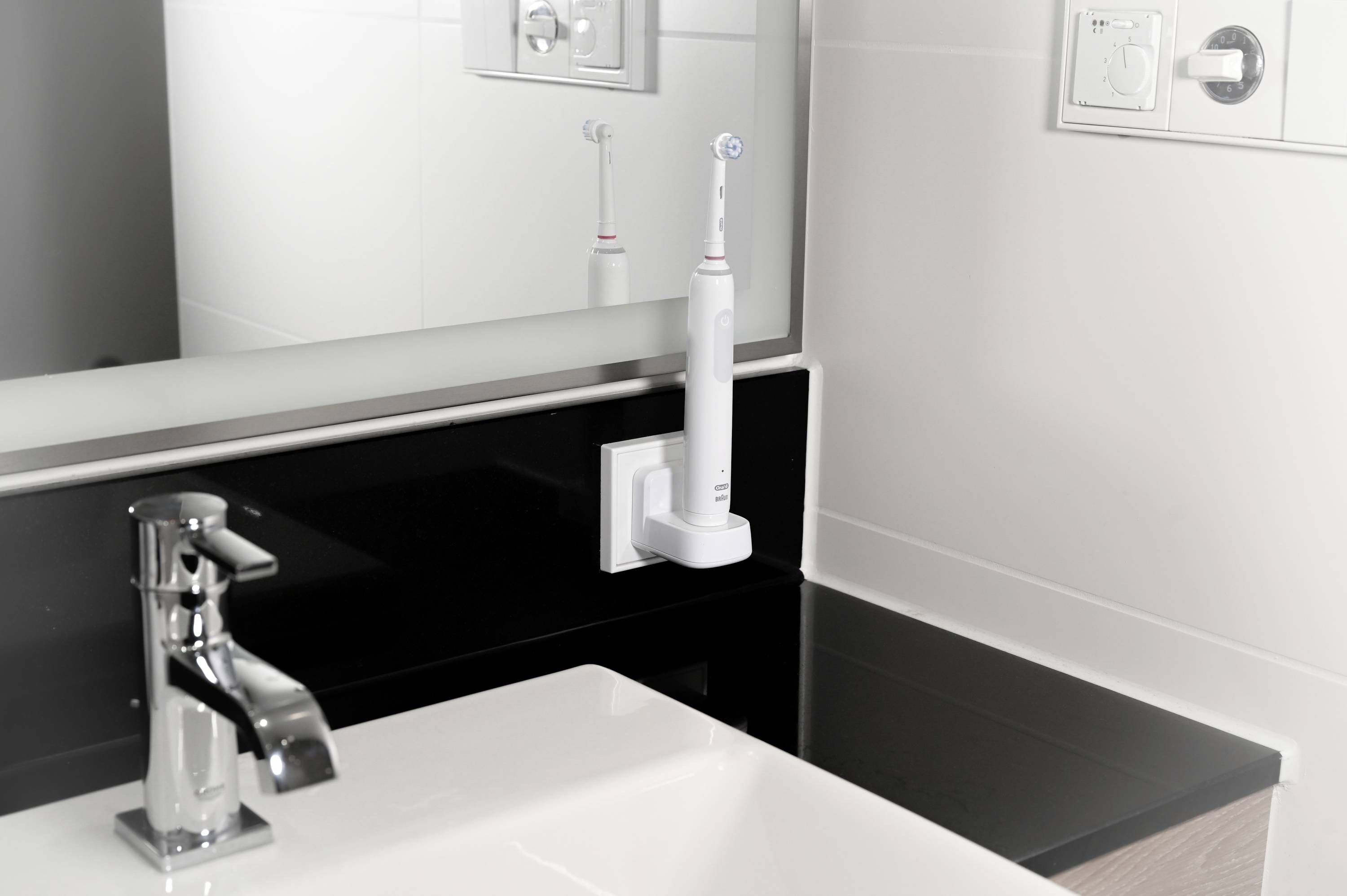 Elektrische Zahnbürste auf Ladestation neben Waschbecken, Spiegel im Hintergrund reflektiert die Bürste.
