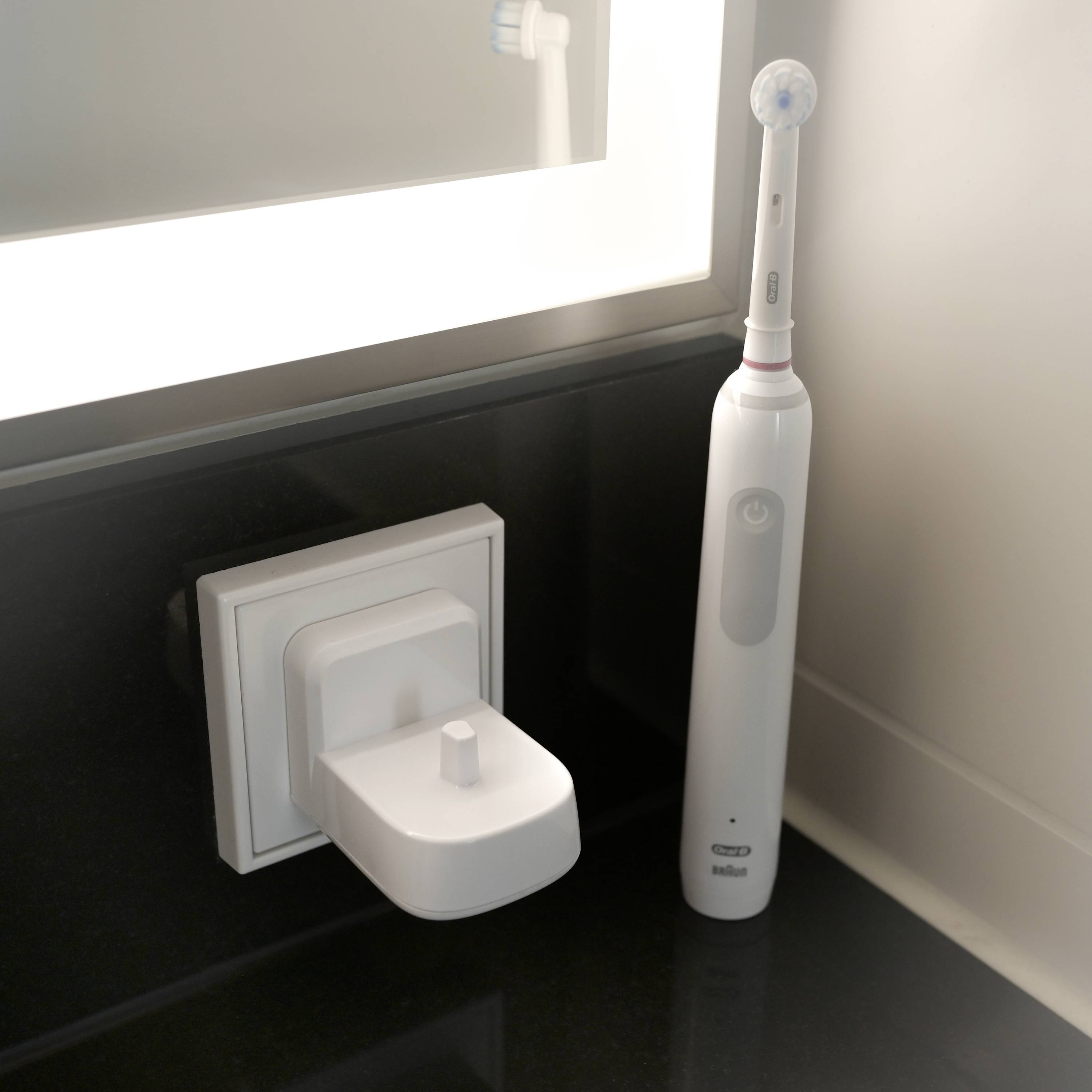 Elektrische Zahnbürste steht in einem Ladedock auf einem Waschbecken neben einem beleuchteten Spiegel.