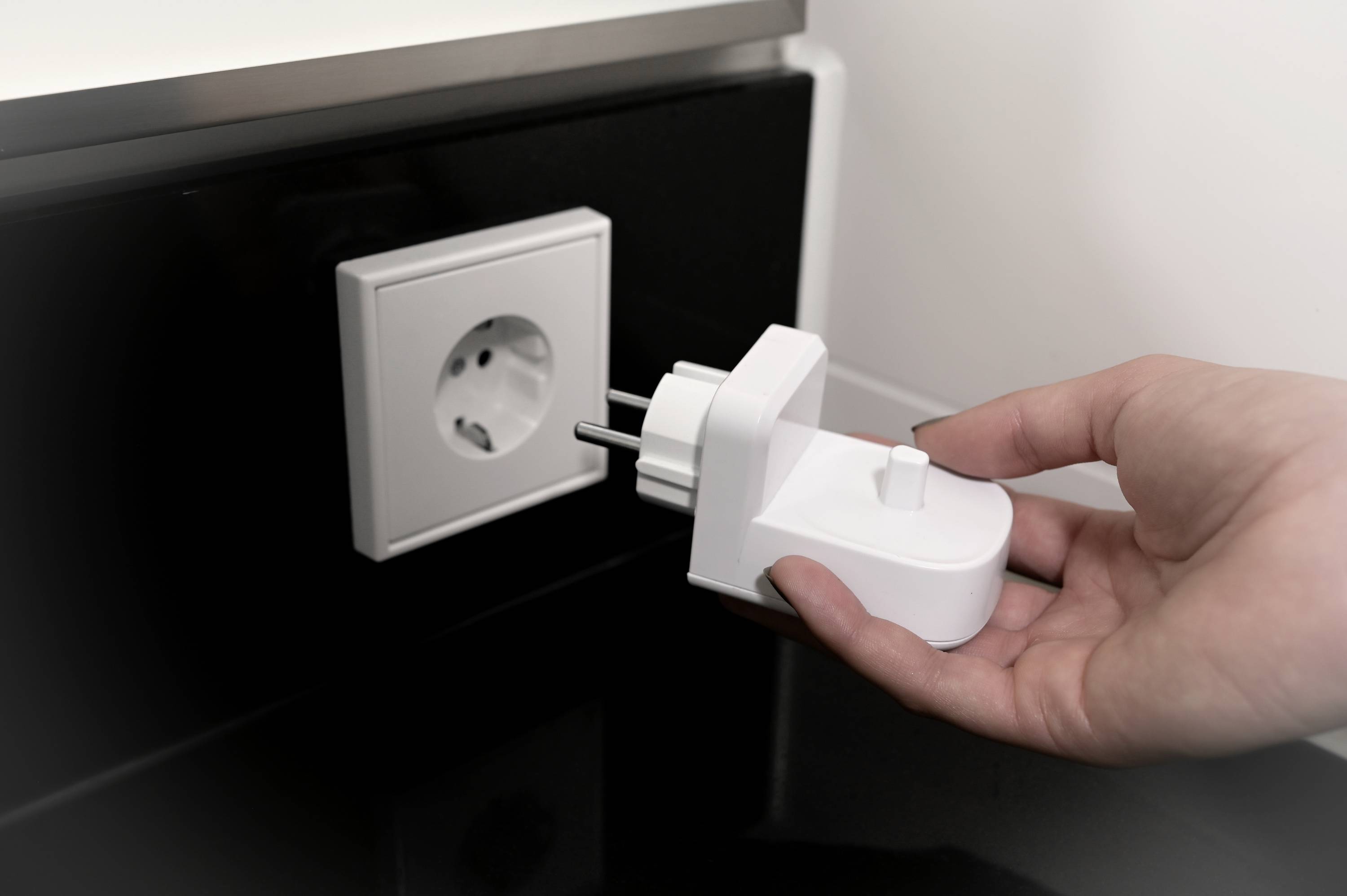 Eine Hand steckt einen weißen Stecker in eine Wandsteckdose.
