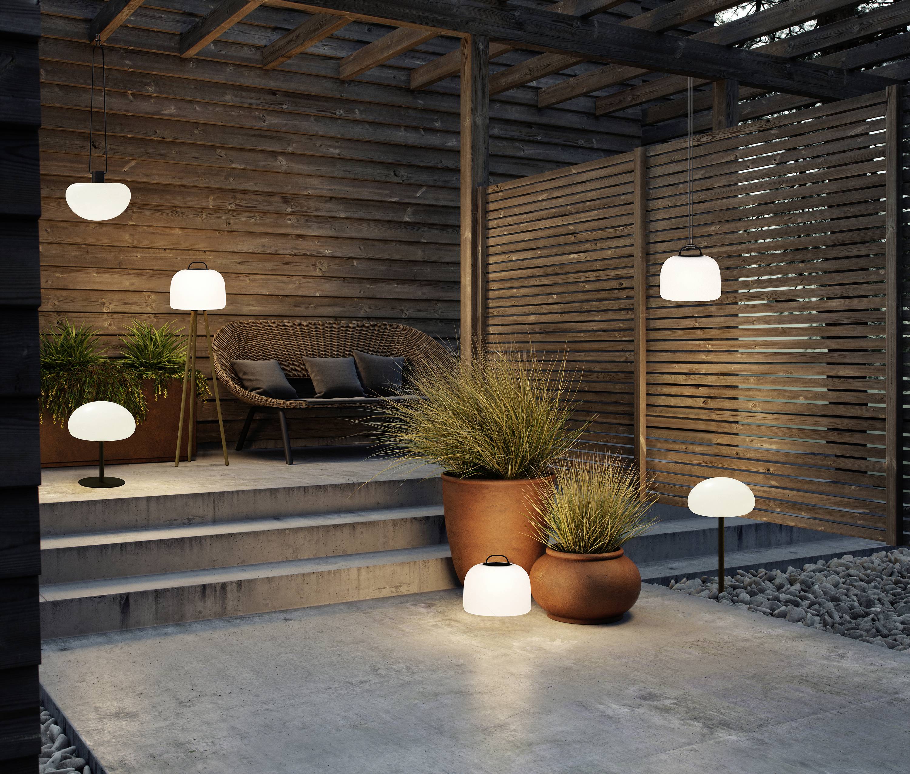 Gemütlicher Holzterrassenbereich mit Sitzmöbeln, umgeben von Pflanzen in Töpfen und mehreren Wegeleuchten für stimmungsvolle Beleuchtung.