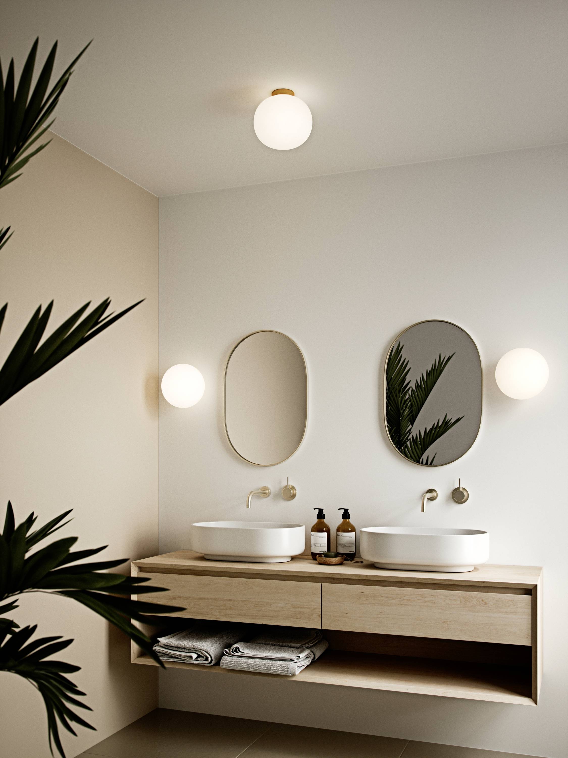 Ein modernes Badezimmer mit Doppelwaschbecken, ovalen Spiegeln und hölzernem Waschtisch. Grüne Pflanze im Vordergrund.