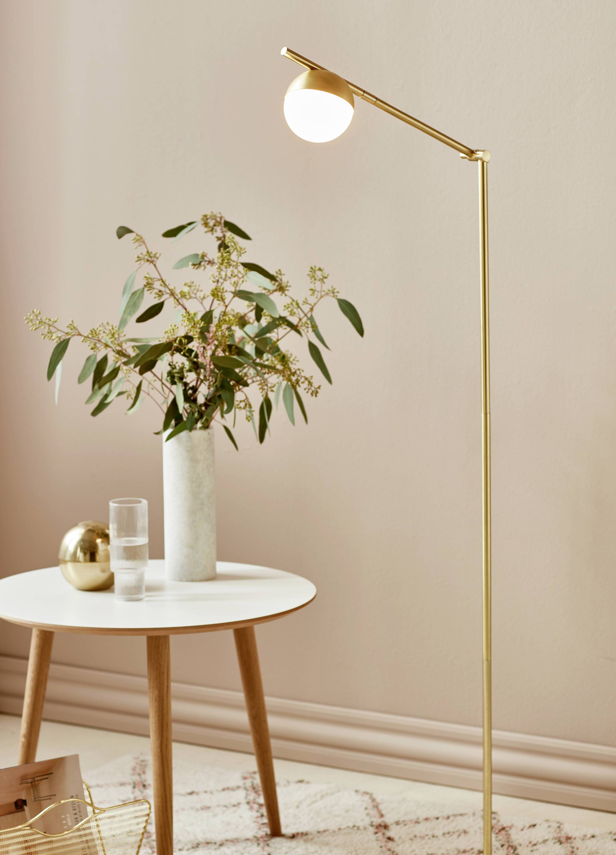 Ein Tisch mit einer dekorativen Vase voller Blumen, ein Glas Wasser, eine goldene Kugel und eine goldene Stehlampe in einem gemütlichen Raum.