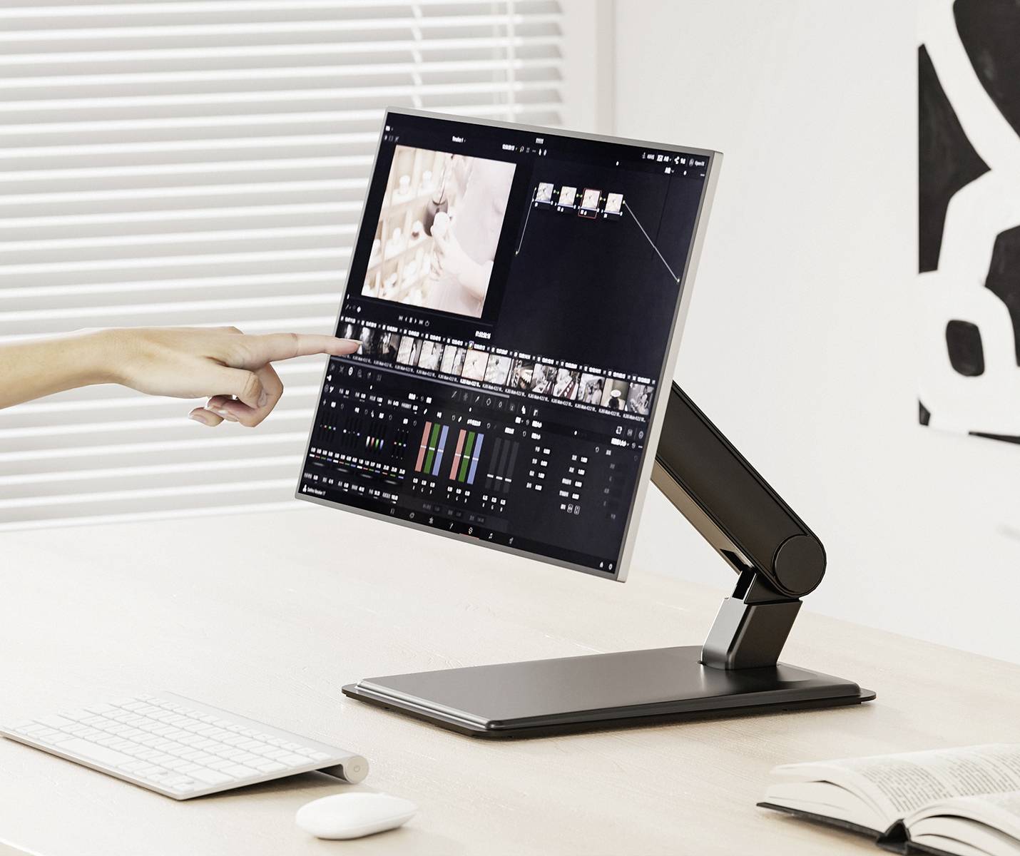 Eine Hand zeigt auf einen Monitor mit einer Videobearbeitungssoftware auf einem Schreibtisch. Im Hintergrund sind Jalousien zu sehen.