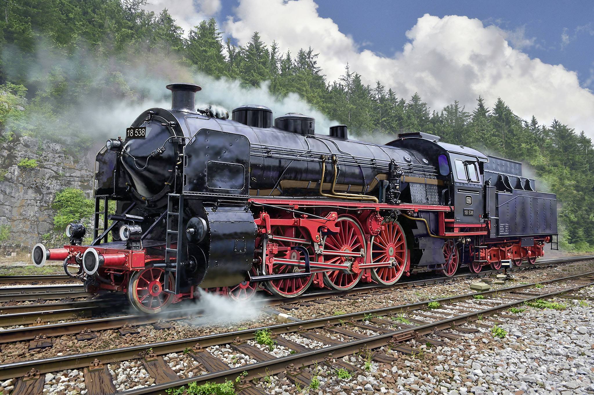 Alte Dampflokomotive auf Schienen, umgeben von bewaldeten Hügeln und blauem Himmel mit Wolken. Rauch steigt aus dem Schornstein.