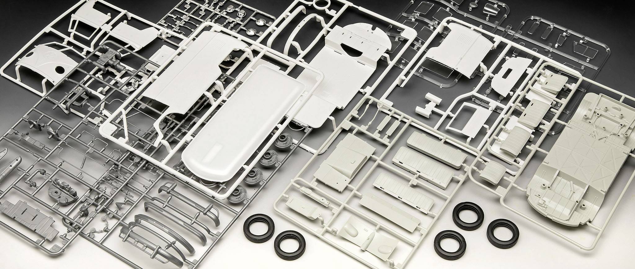 Plastikmodellbausatz eines Fahrzeugs, bestehend aus grauen und weißen Rahmen mit Einzelteilen sowie kleinen Gummireifen.