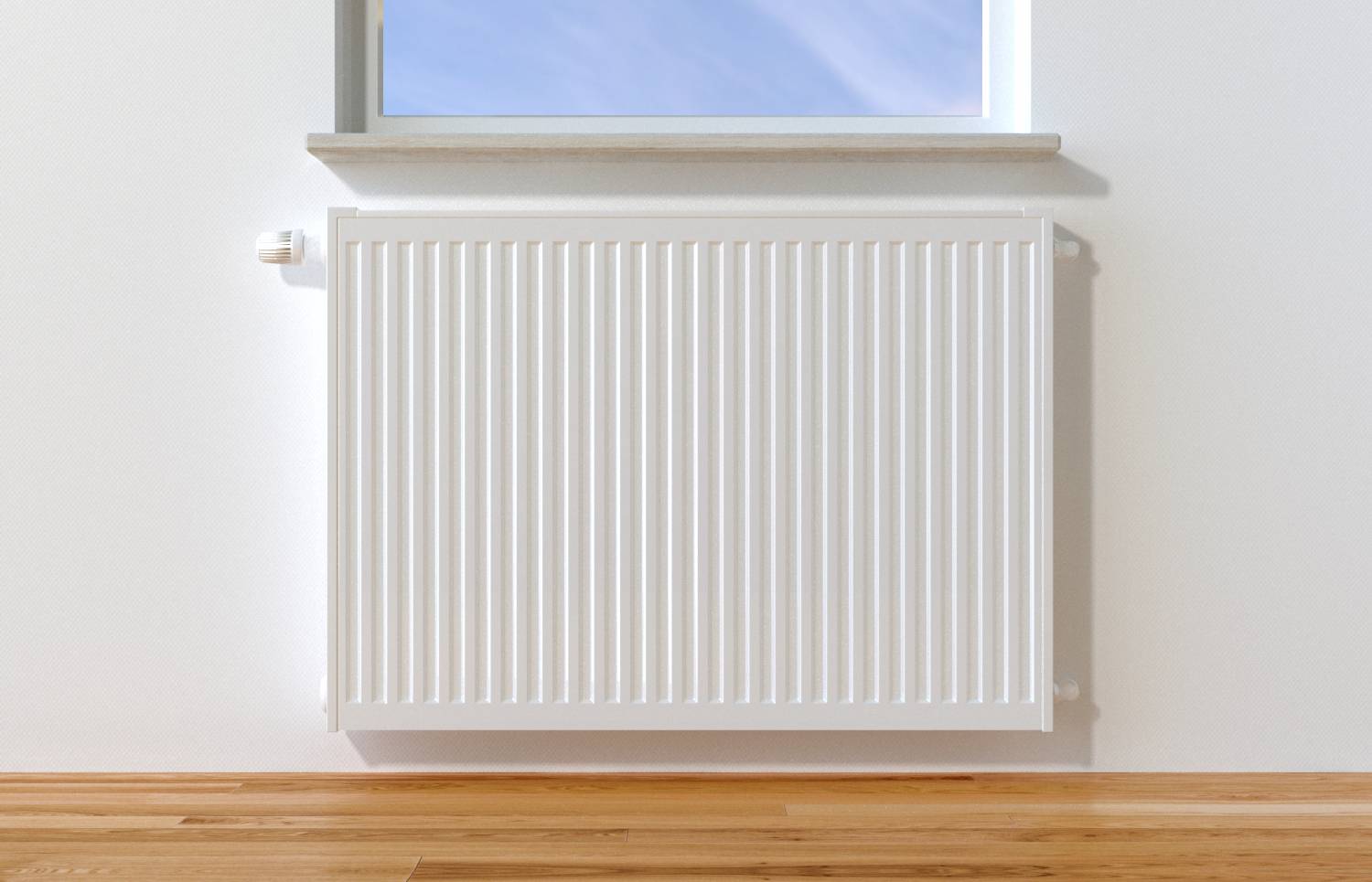 Ein weißer Heizkörper an einer Wand unter einem Fenster, durch das blauer Himmel sichtbar ist. Holzboden darunter.