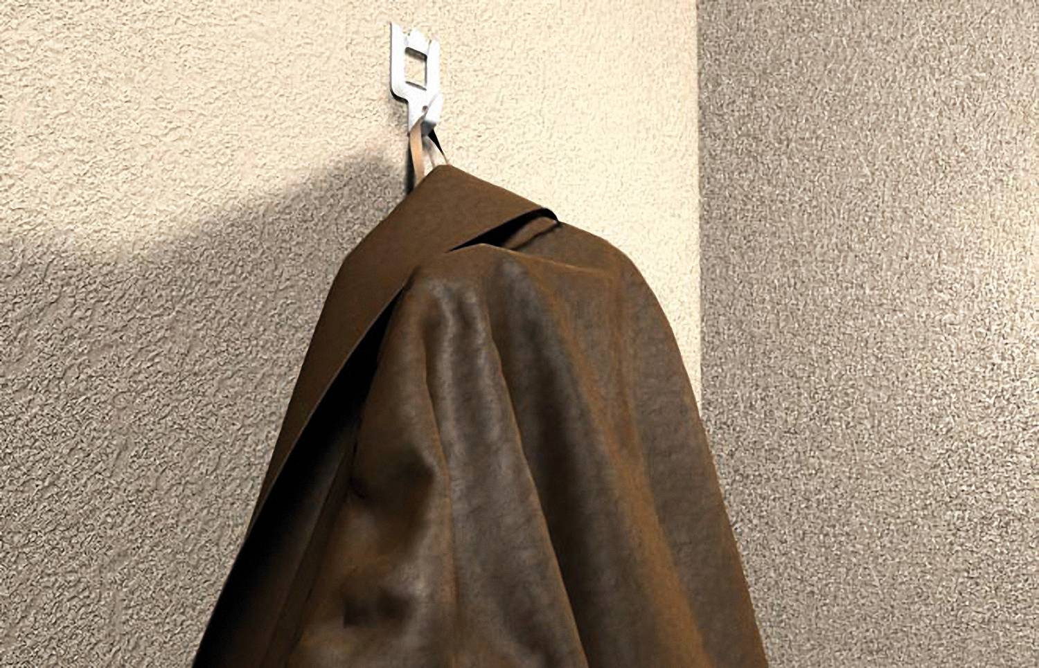Ein brauner Mantel hängt an einem Wandhaken an einer strukturierten beigefarbenen Eckwand.
