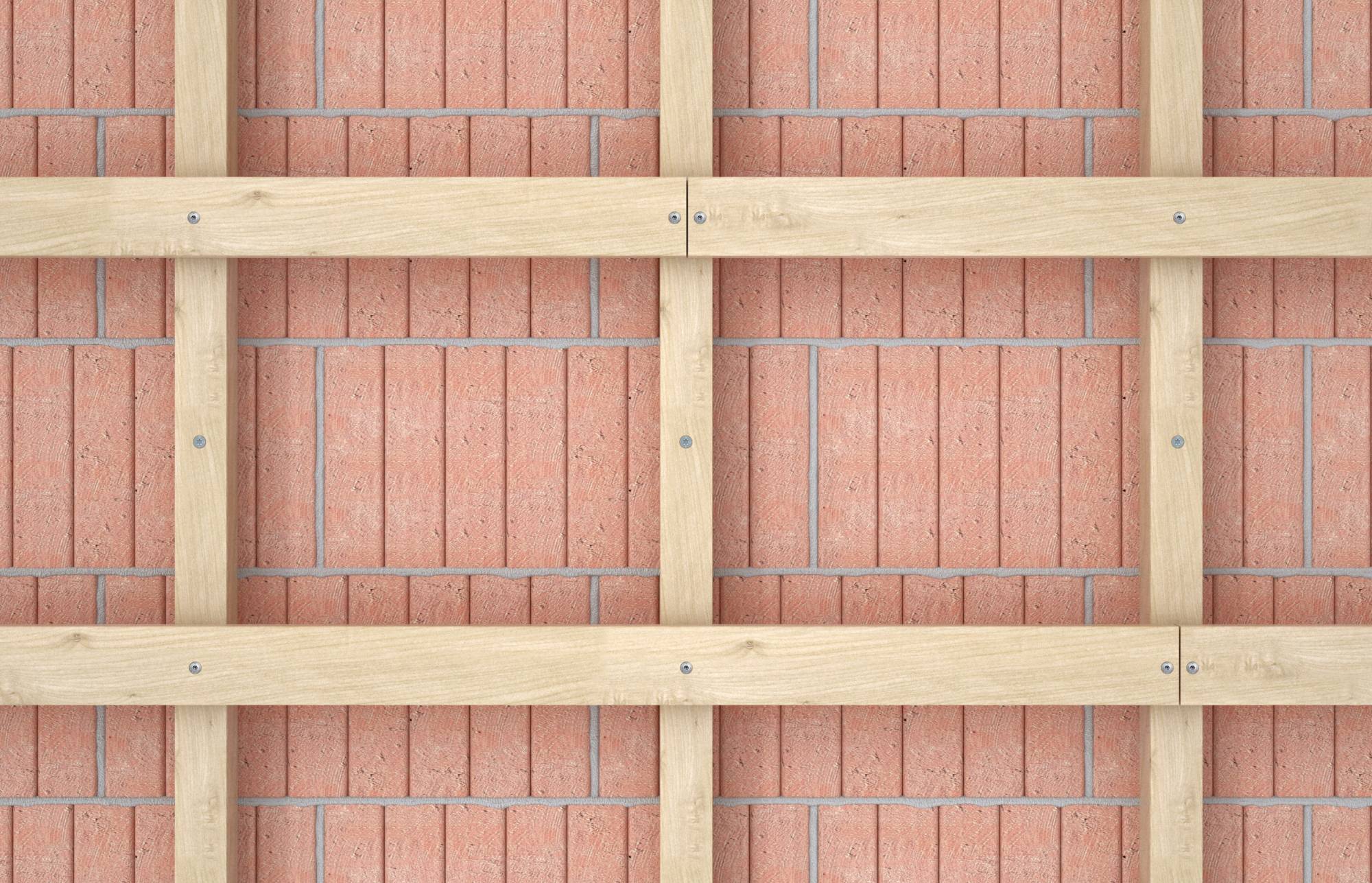 Eine Holzrahmenkonstruktion überdeckt eine rote Ziegelwand, sichtbar sind quadratische Felder aus Holzlatten, gleichmäßig verteilt.
