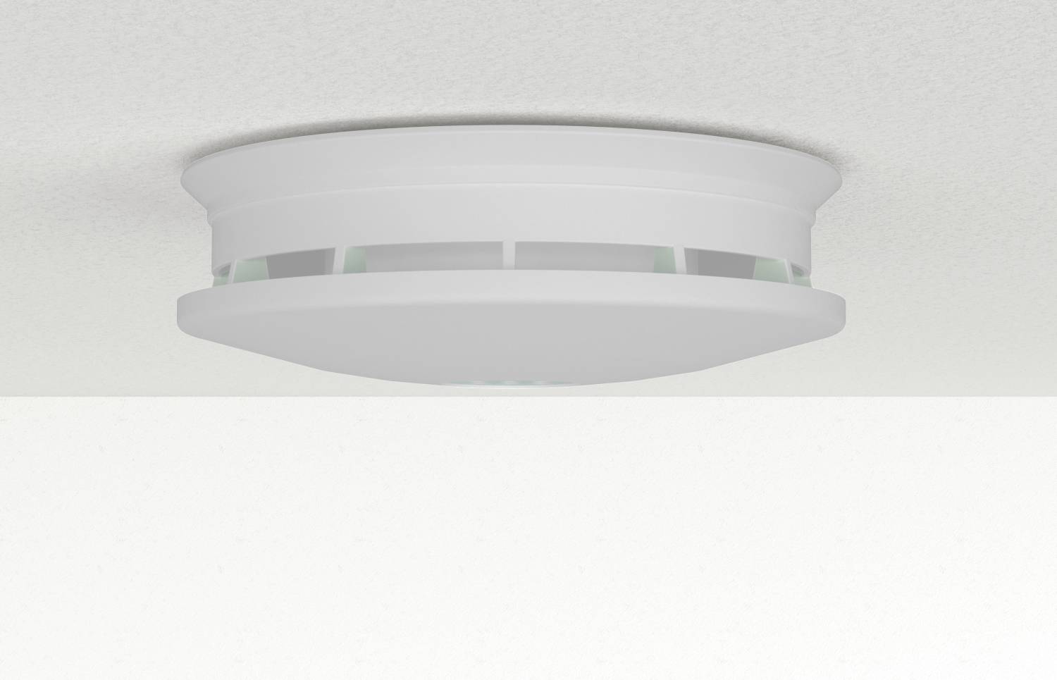 Weißer runder Rauchmelder an einer Decke vor einem einfachen Hintergrund angebracht.