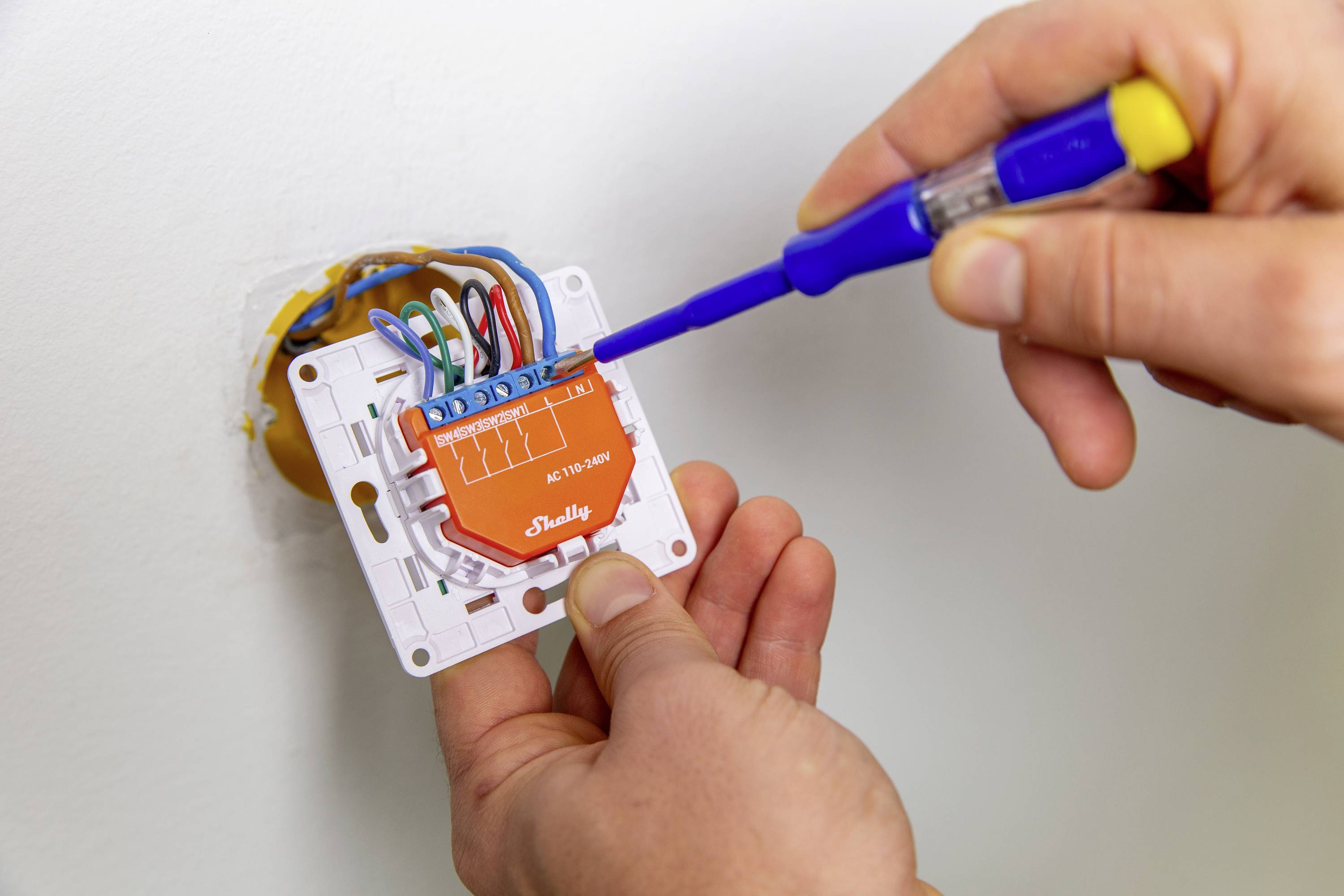 Person montiert einen elektrischen Schalter mit einem Schraubendreher. Mehrere Kabel sind angeschlossen.