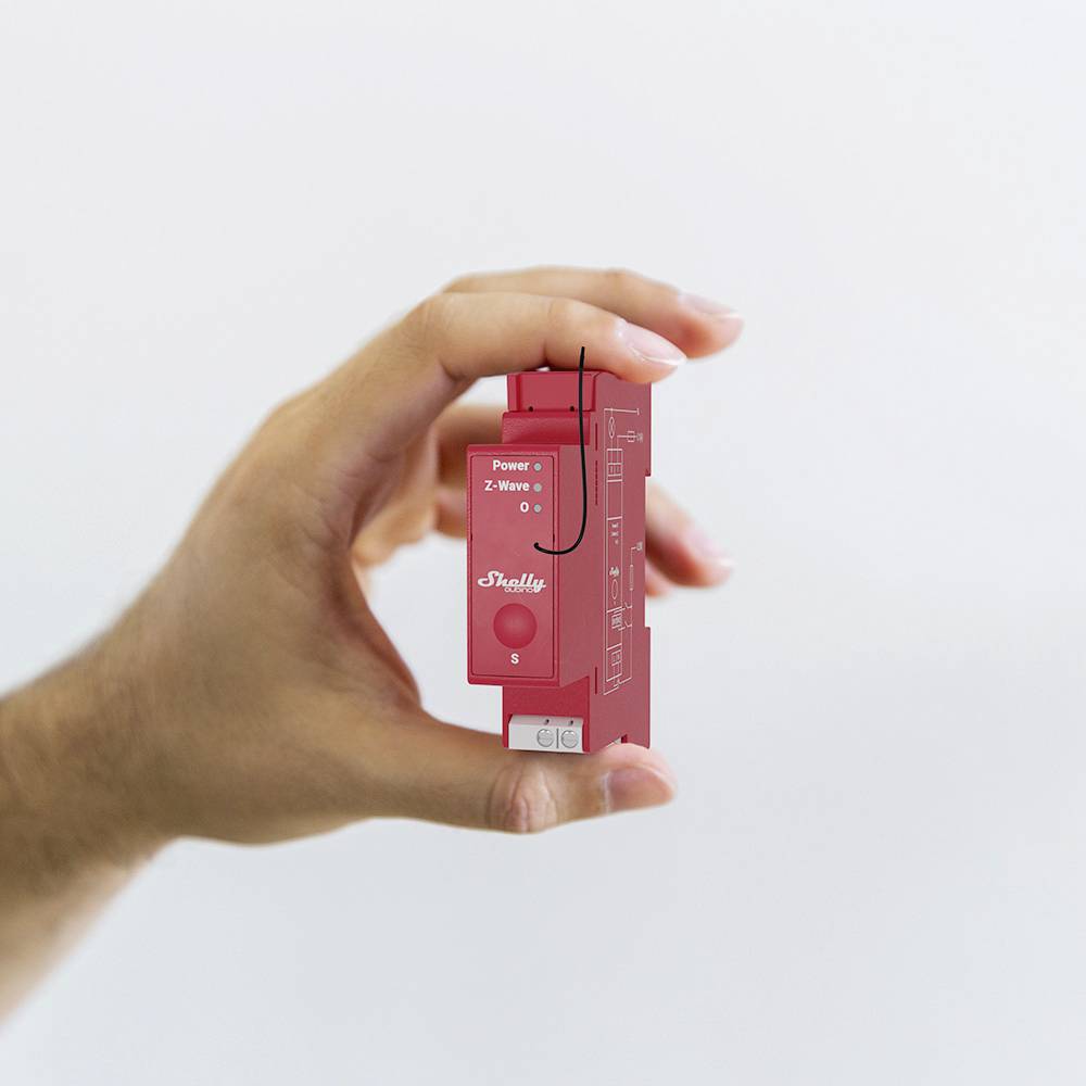 Eine Hand hält ein kleines, rotes Gerät mit der Aufschrift 'Shelly'. Es ist ein elektrisches Bauteil, vermutlich ein Smart-Home-Schalter.