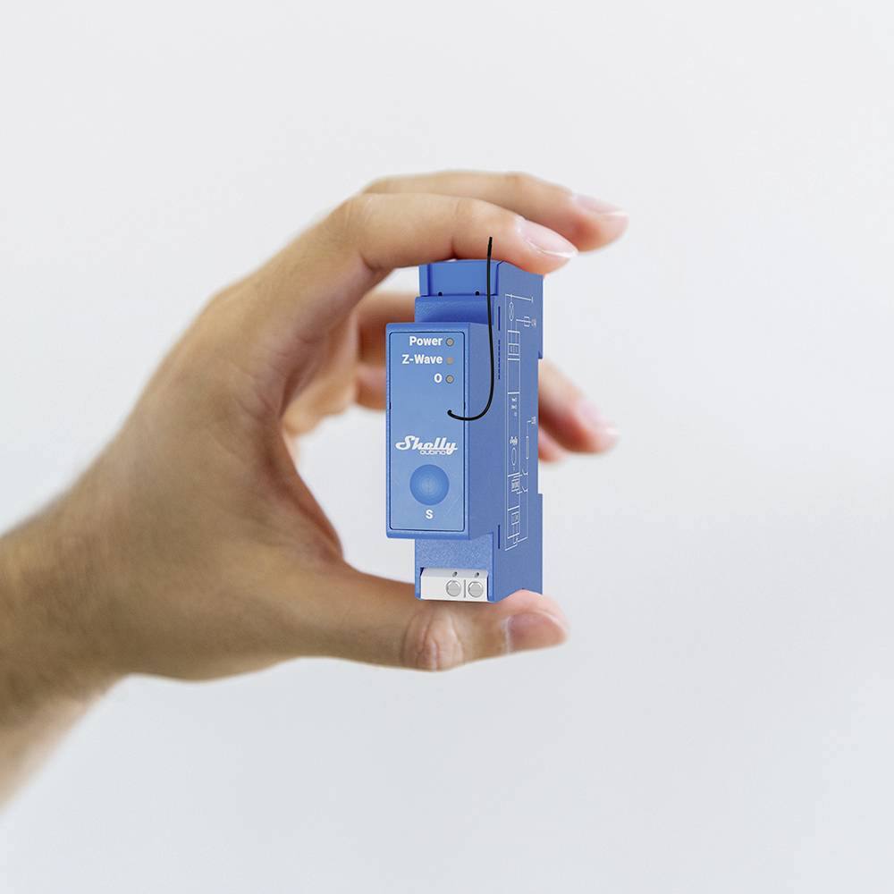 Eine Hand hält einen blauen elektrischen Schalter. Auf dem Gerät steht 'Shelly' und es hat LEDs für 'Power' und 'Z-Wave'.