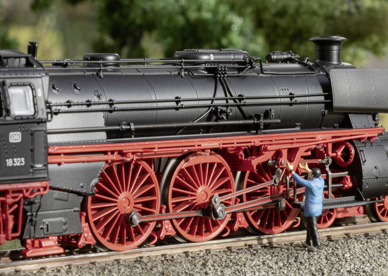 Ein Miniaturfigurenmodell eines Mannes steht neben einem schwarzen Dampflokmodell mit roten Rädern im Freien.