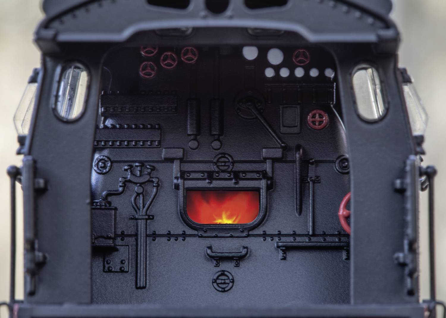 Blick in die Fahrerkabine einer Dampflok mit sichtbarem Feuer im Ofen, umgeben von Hebeln und Ventilen zur Steuerung.