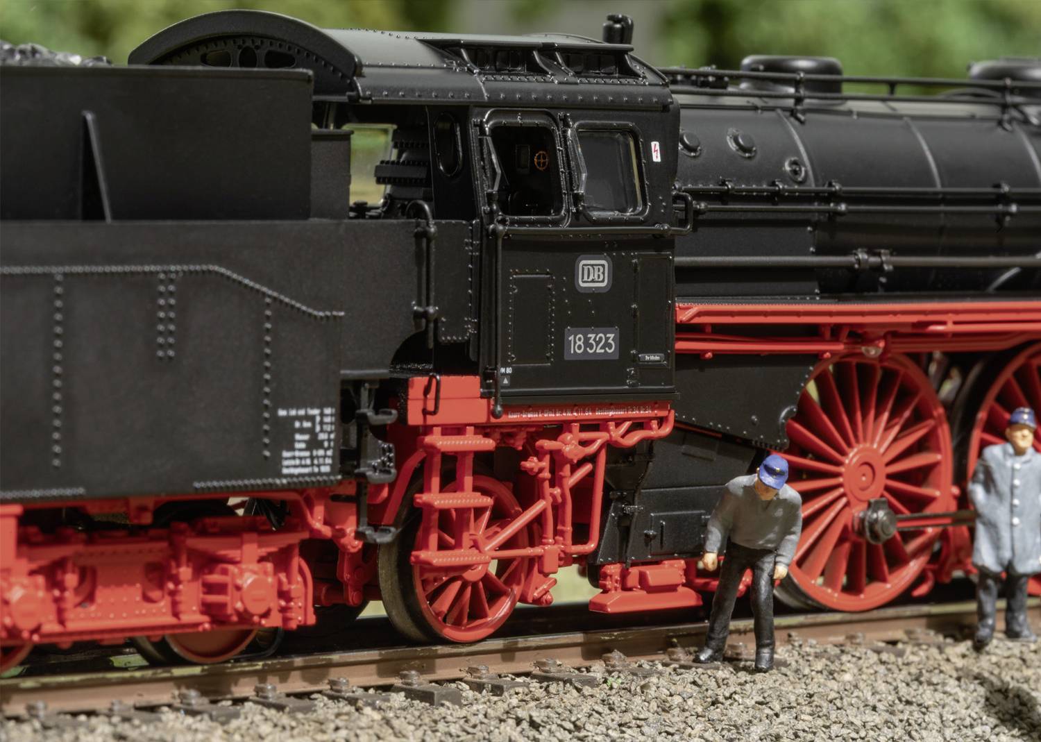 Altes Lokomotivmodell der Deutschen Bahn in Schwarz und Rot, zwei Figuren in Arbeitskleidung stehen daneben auf einem Gleis.