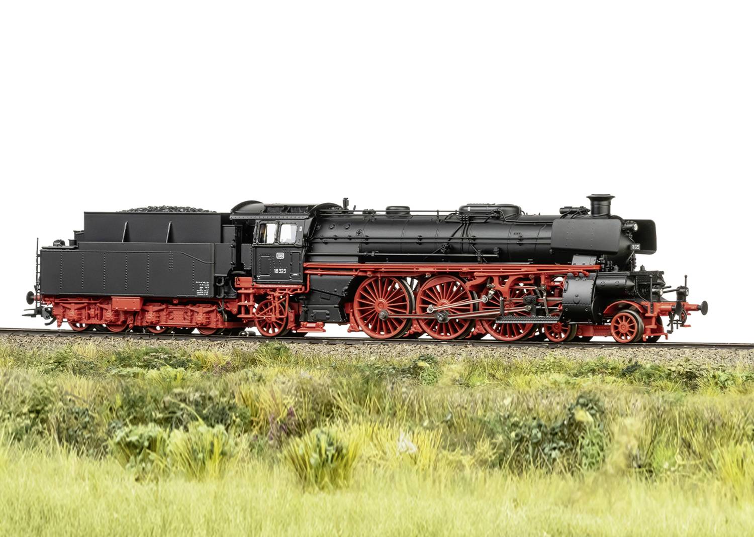 Eine schwarze Dampflokomotive mit roten Rädern und Details steht auf Schienen, umgeben von Grasbewuchs.