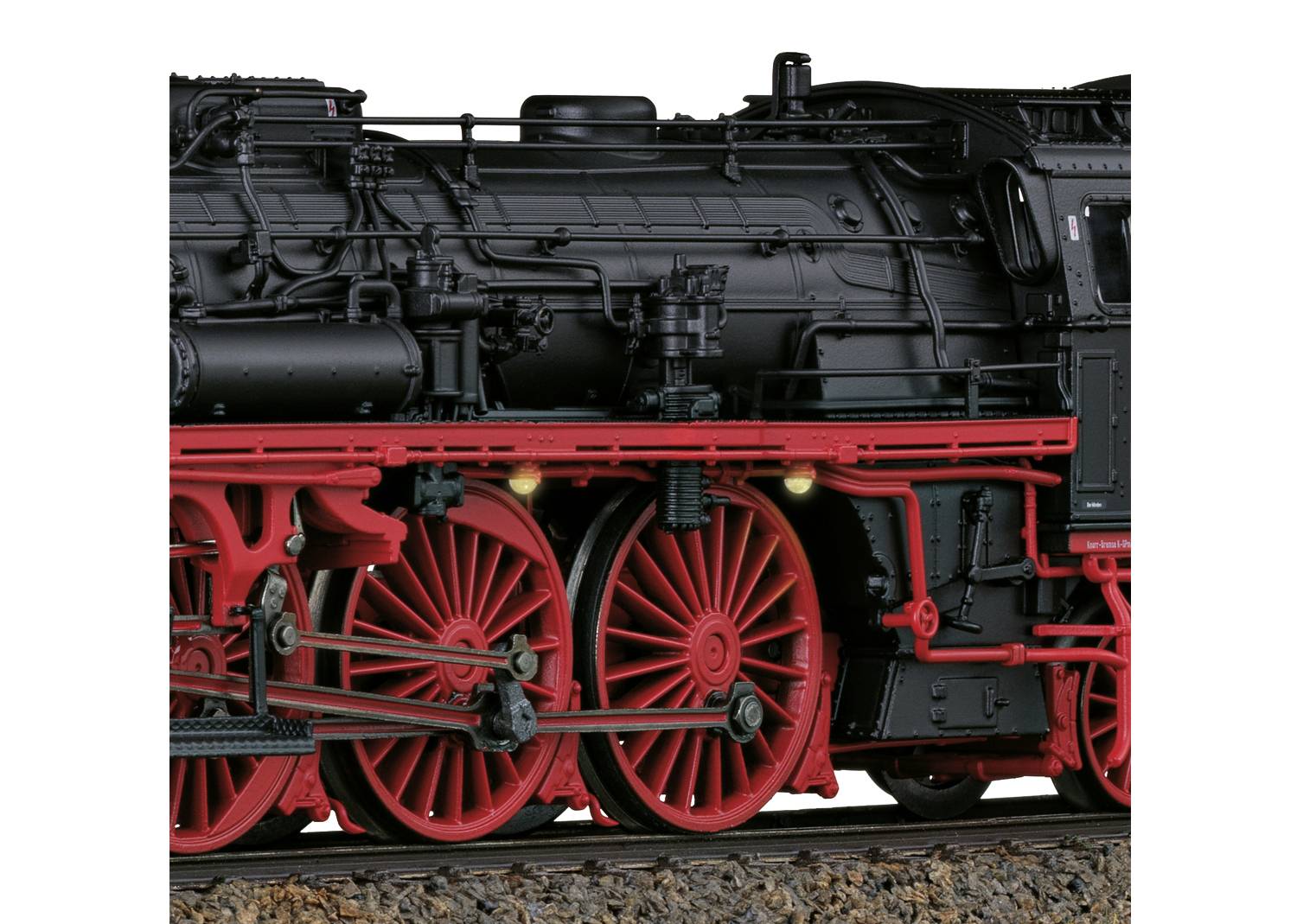 Nahaufnahme einer historischen Dampflokomotive. Schwarzer Kessel mit roten Speichenrädern auf Schienen. Mechanische Details sichtbar.