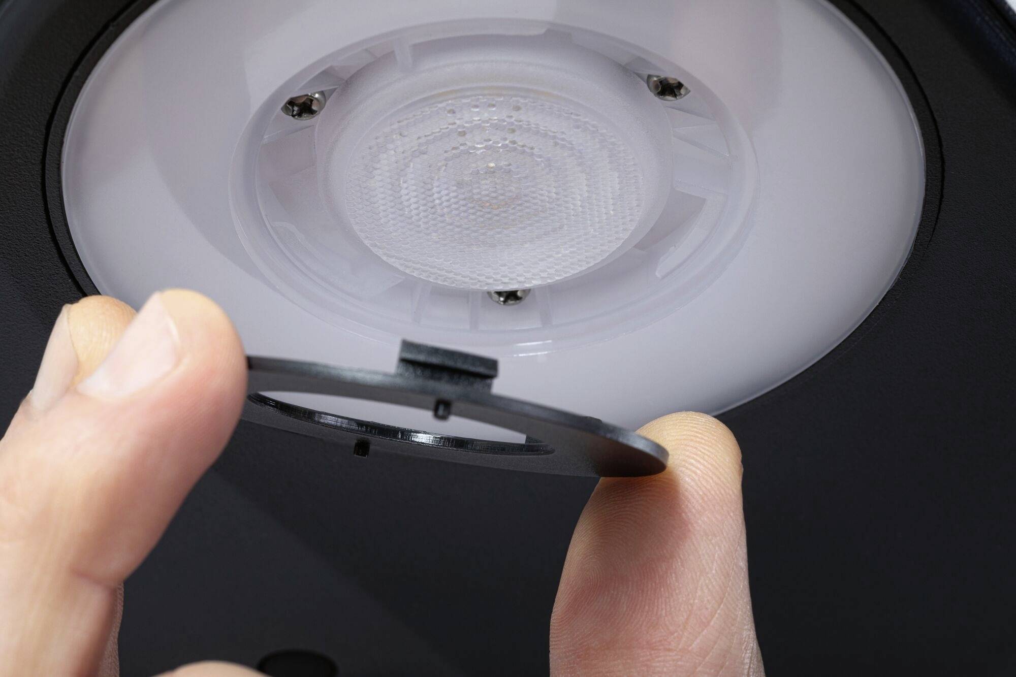 Eine Hand hält eine schwarze Abdeckung unter einem runden, eingebauten LED-Deckenlicht.