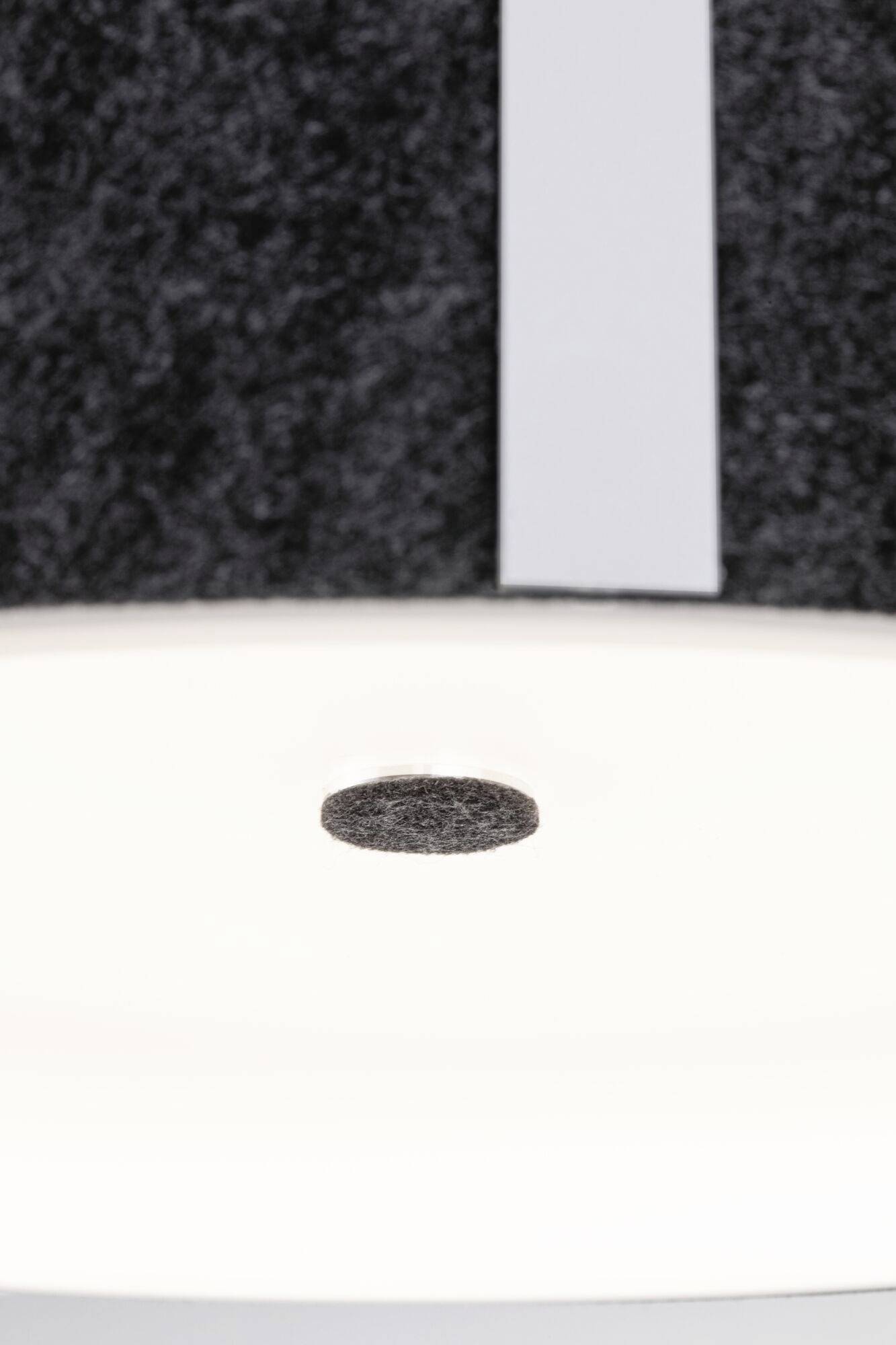 Eine runde, isolierte Filzscheibe schwebt knapp über einer hellen, weißen Fläche, vor einem dunklen, texturierten Hintergrund.