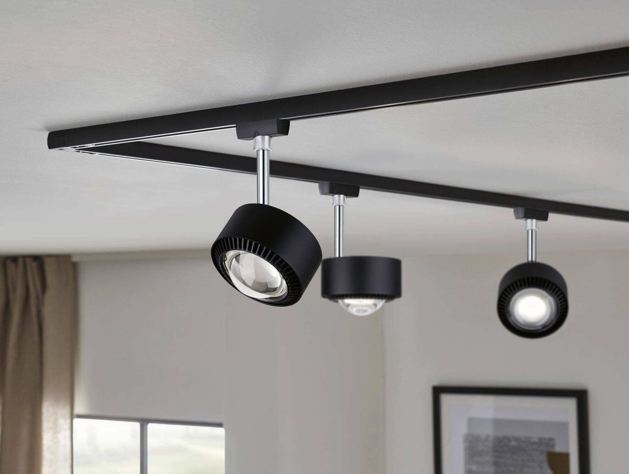 Drei schwarze LED-Deckenspots sind an einer Schiene montiert. Sie leuchten einen Bereich in einem modernen Innenraum aus.