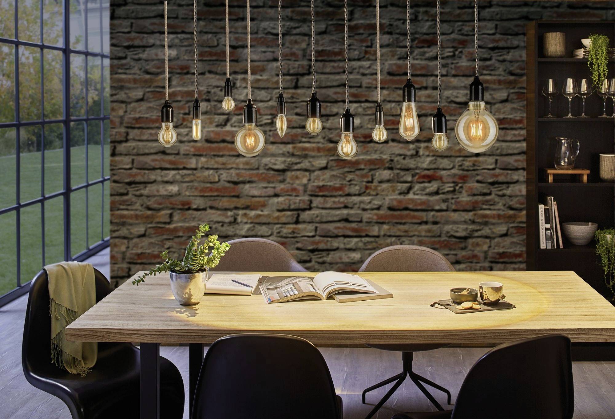 Esszimmer mit hellem Holztisch, umgeben von schwarzen Stühlen. Viele Hängeleuchten hängen darüber, eine Stimmung von Gemütlichkeit erweckend.