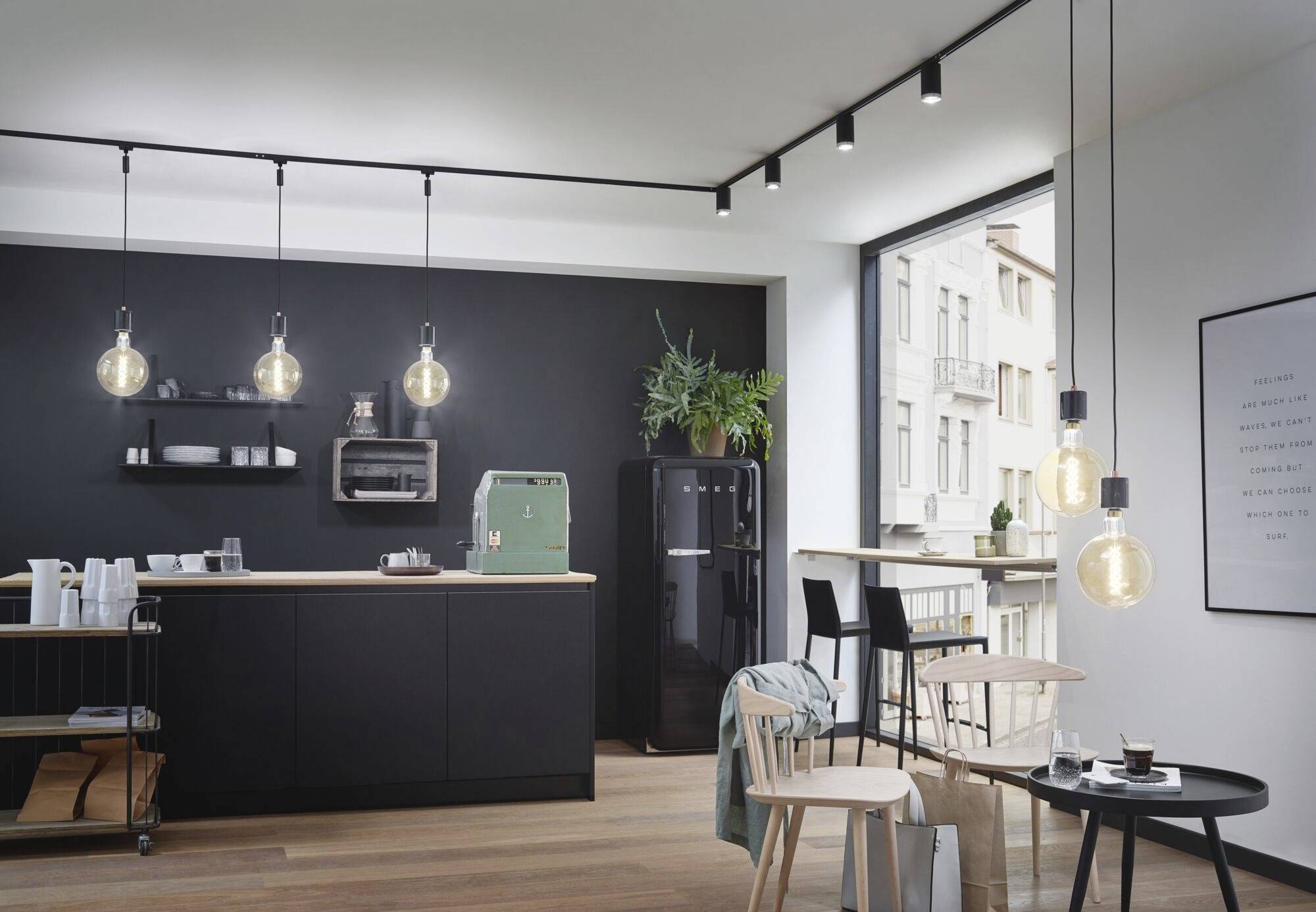 Moderne Küche mit schwarzer Einrichtung und hängenden Glühbirnen. Eine grüne Kaffeemaschine steht auf der Arbeitsplatte.