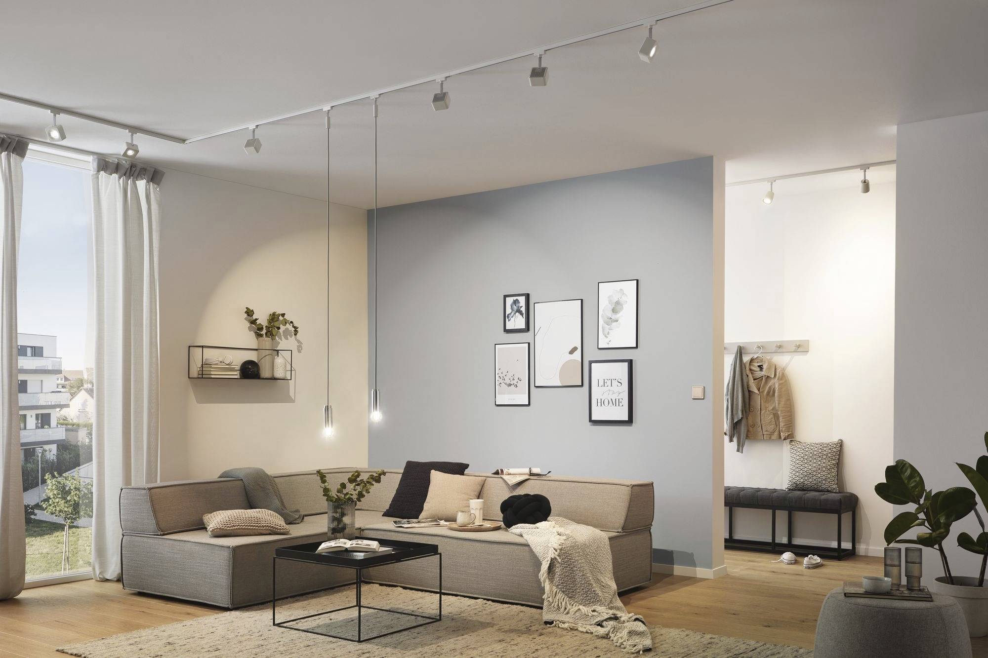 Modernes Wohnzimmer mit grauem Sofa, Couchtisch, hellem Holzfußboden und blauen Wänden, dekoriert mit Bildern und Pflanzen.
