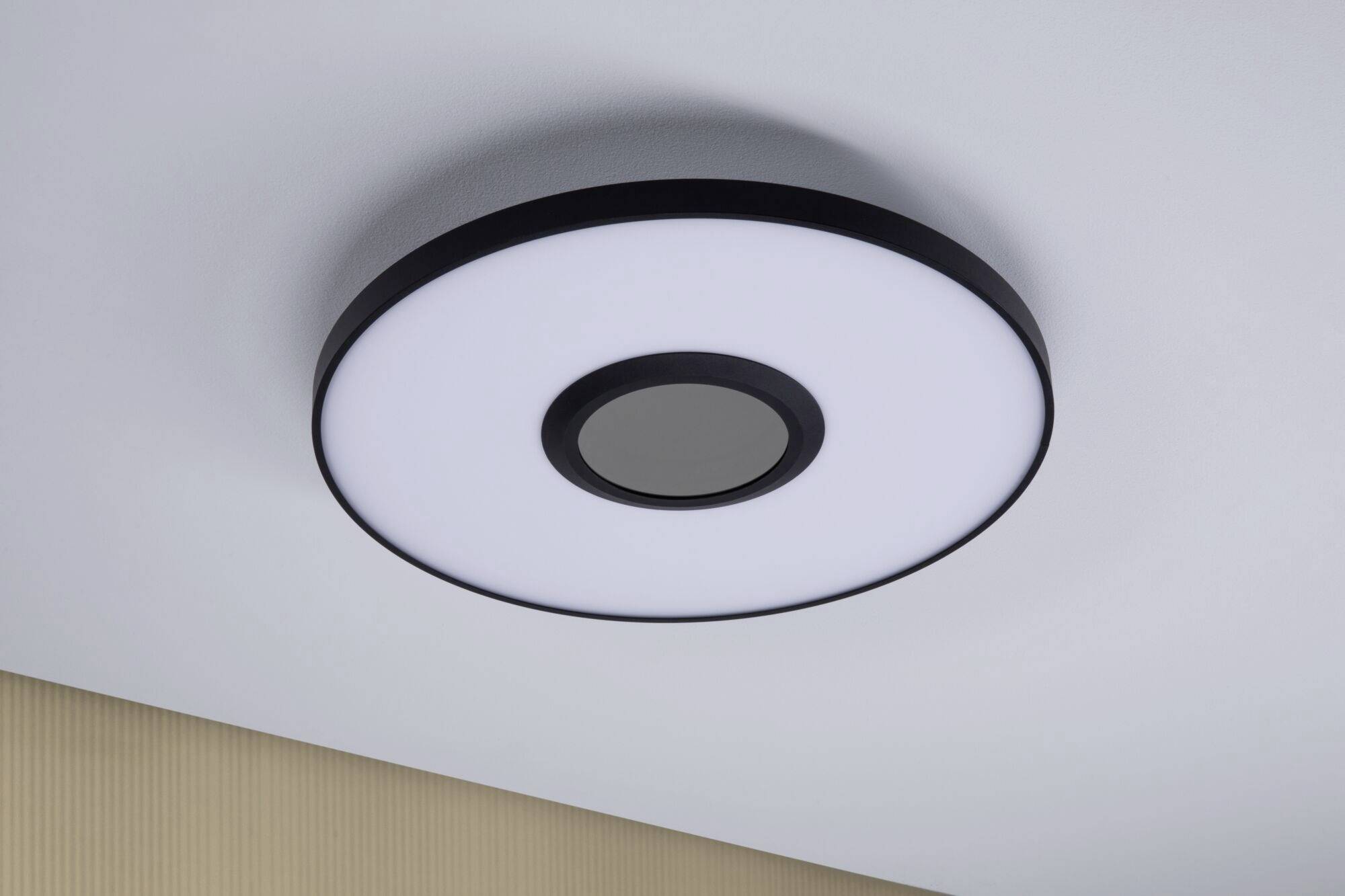 Runde moderne Deckenlampe mit schwarzem Rand, zentraler Diffusor und heller Leuchtfläche, montiert an einer weißen Decke.