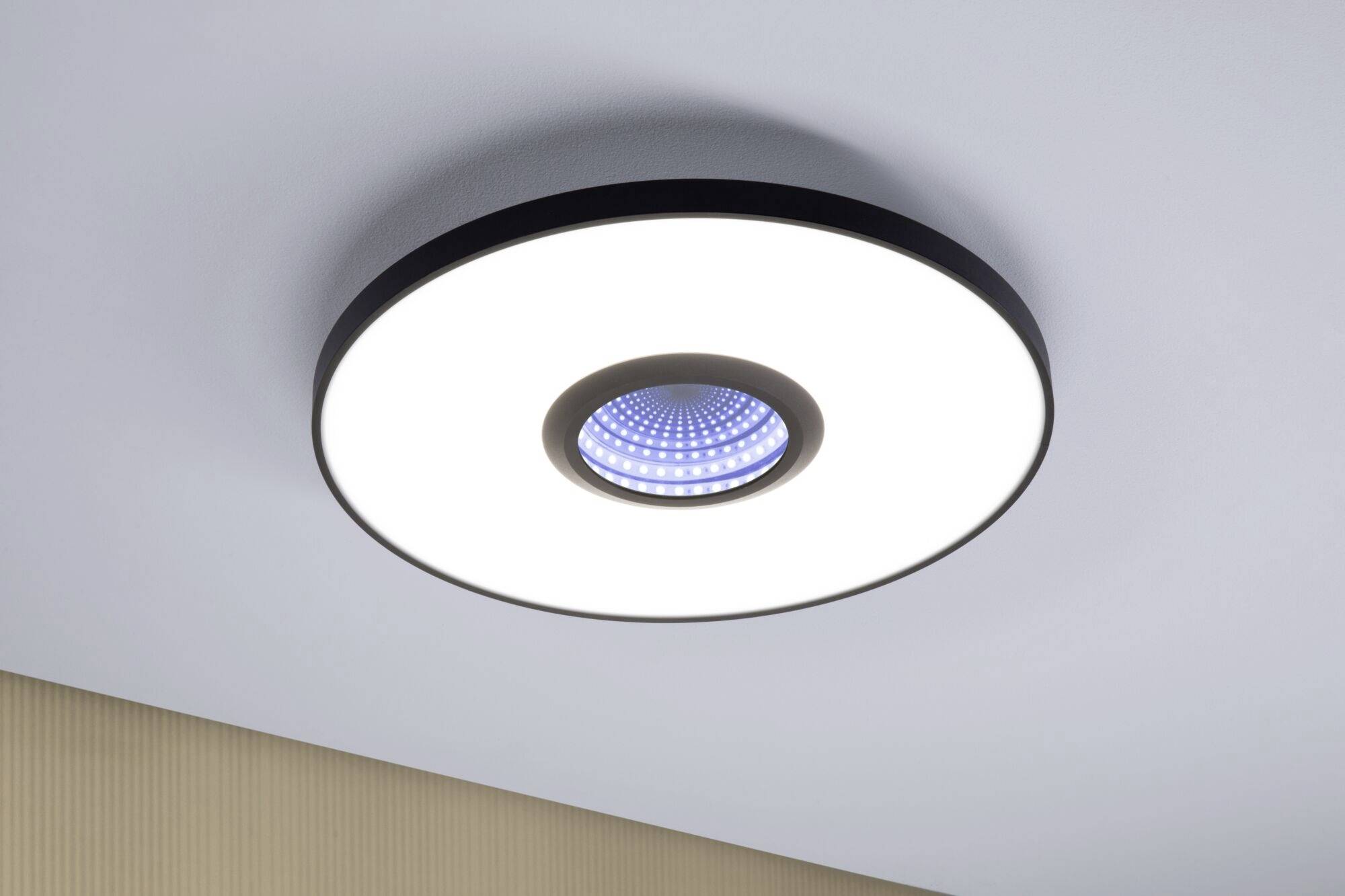 Eine runde Deckenleuchte mit einem zentral blauen LED-Element, montiert an einer weißen Decke, spendet helles Licht.