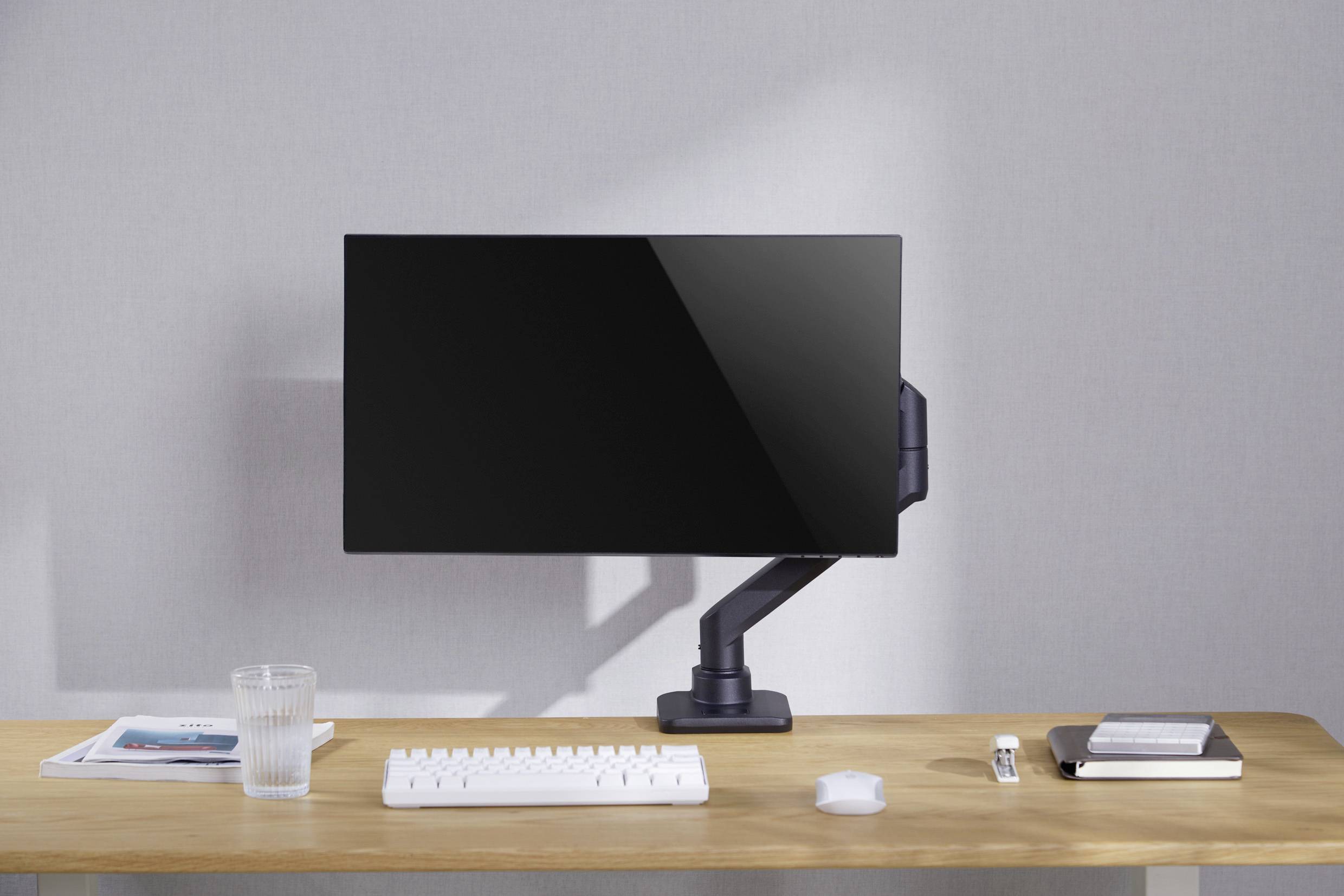 Ein Schreibtisch mit einem Monitor, einer Tastatur, einem Glas Wasser, einer Maus, einigen Büchern und einem Notizheft. Der Monitor ist ausgeschaltet.