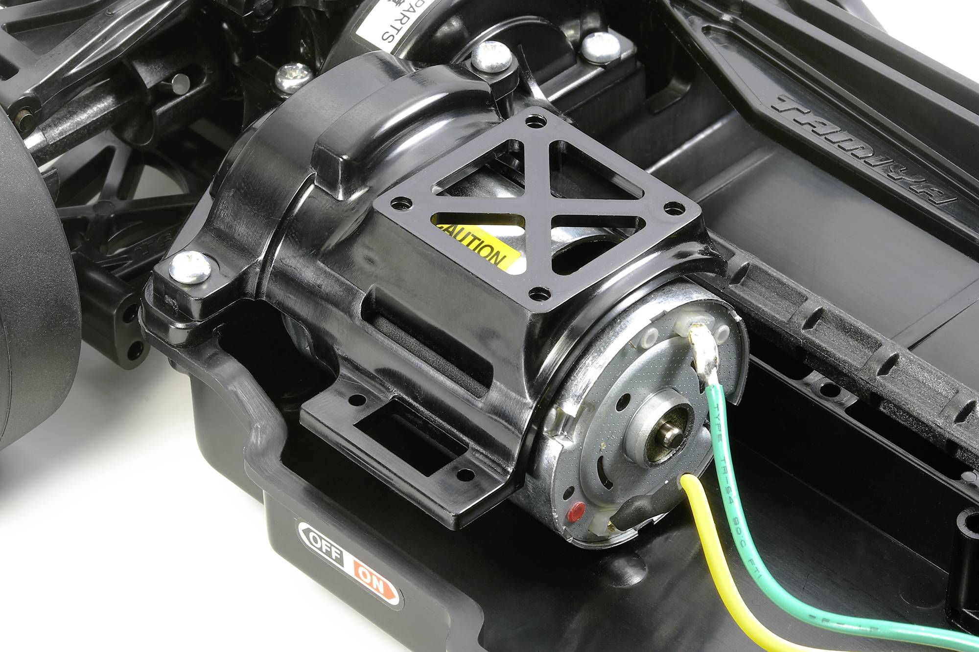 Nahaufnahme eines ferngesteuerten Autogetriebes mit sichtbarem Motor. Gelbes Warnschild auf dem Metallrahmen des Getriebes.