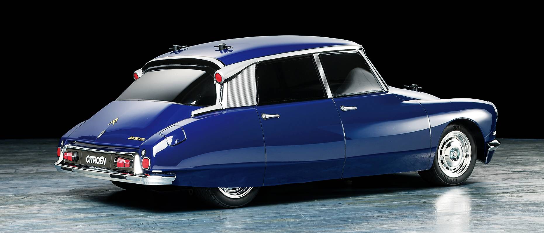 Ein blauer Citroën DS aus den 1960er Jahren, aufgenommen von hinten in einem Studio. Das Auto hat stromlinienförmiges Design und verchromte Details.