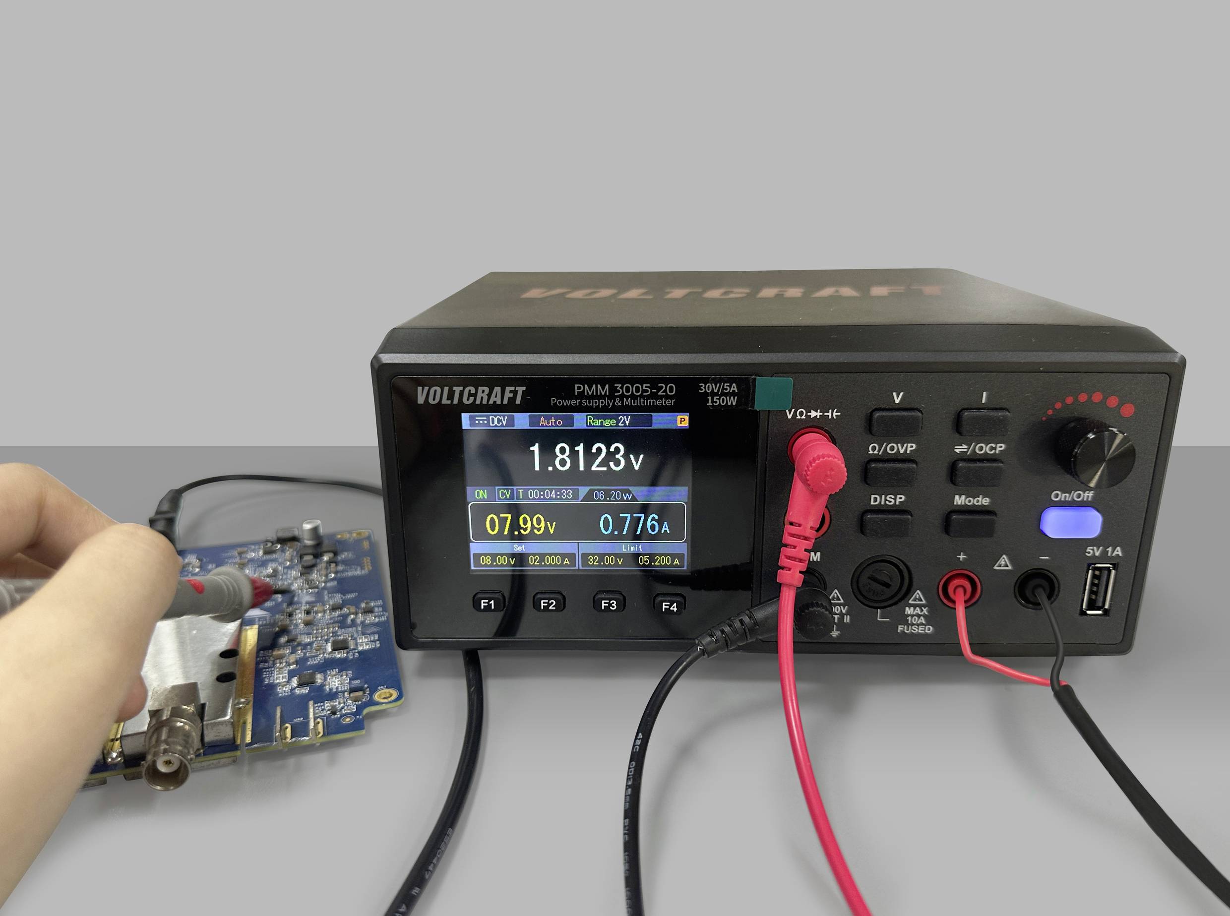 Ein Messgerät zeigt '1,8123 V' und '0,776 A' auf einem digitalen Display, während eine Hand die Spannung an einer Platine testet.