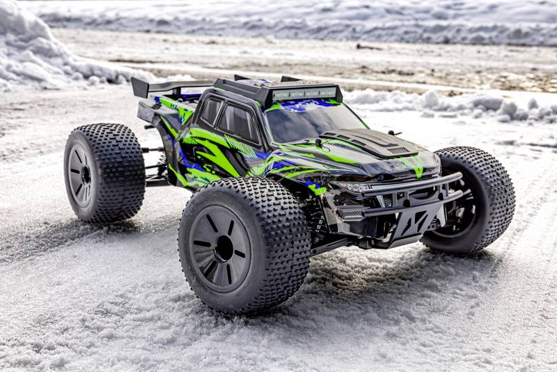 Ein ferngesteuertes, allradgetriebenes Auto mit grün-schwarzem Design steht auf einer schneebedeckten Straße.