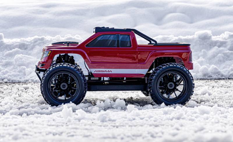 Ein rotes ferngesteuertes Auto steht auf schneebedecktem Boden, umgeben von Schneewehen im Hintergrund.