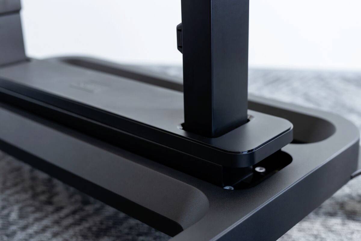 Nahaufnahme einer schwarzen, modernen Schreibtischhalterung für Monitore. Die Halterung ist stabil auf einem grauen Tisch montiert.