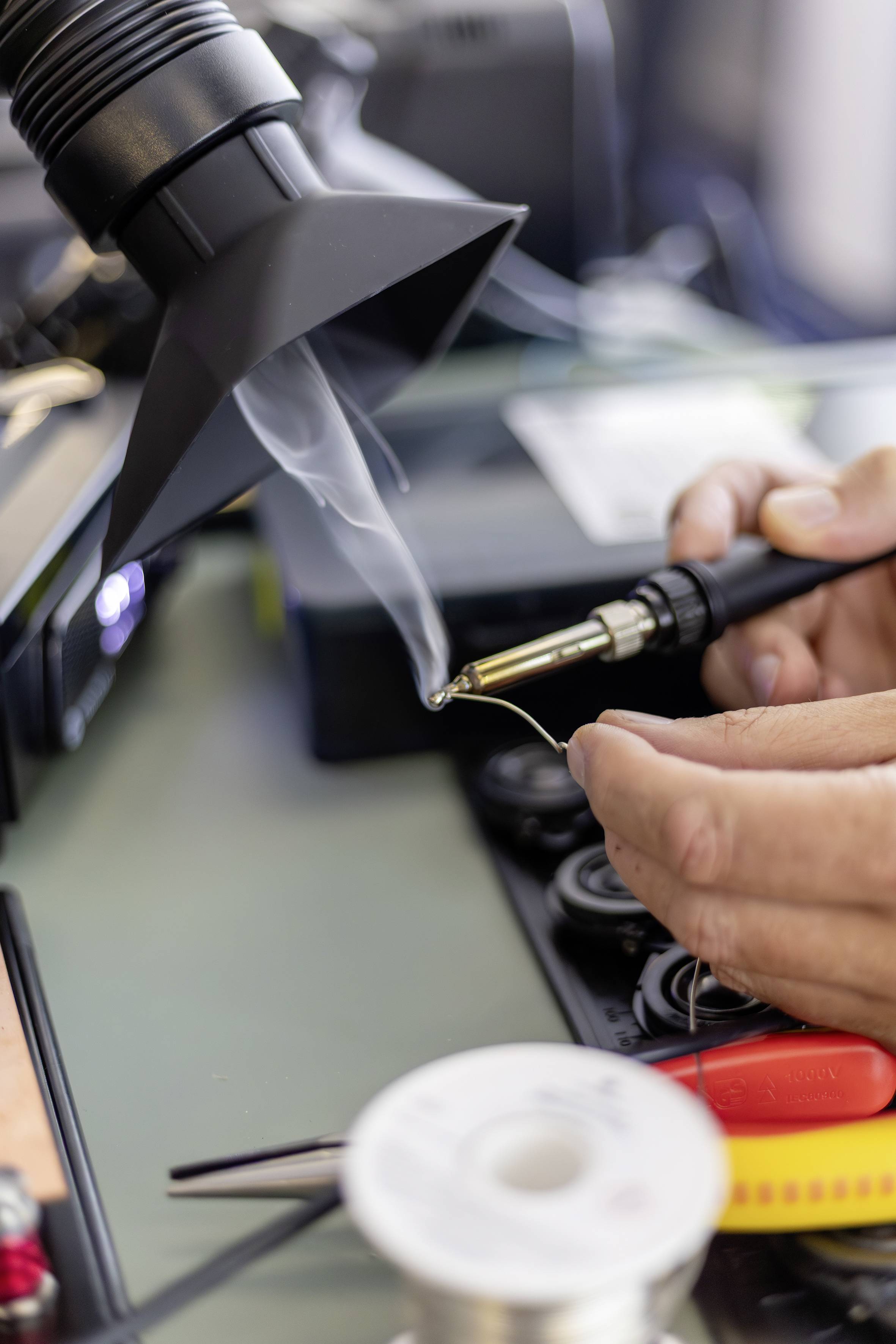 Nahaufnahme einer Person, die Elektronik mit einem Heißluftlöter und Lötkolben an einer Werkbank lötet.