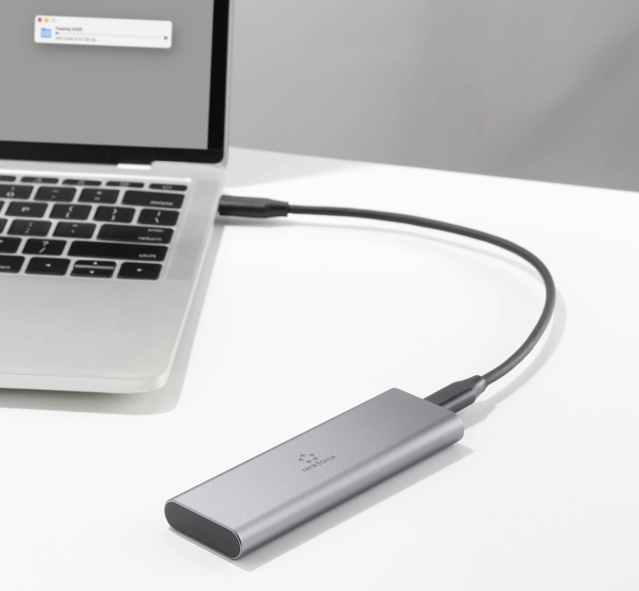 Ein silberner Laptop ist mit einem kleinen, silbernen externen Speichergerät verbunden, das über ein schwarzes Kabel angeschlossen ist.