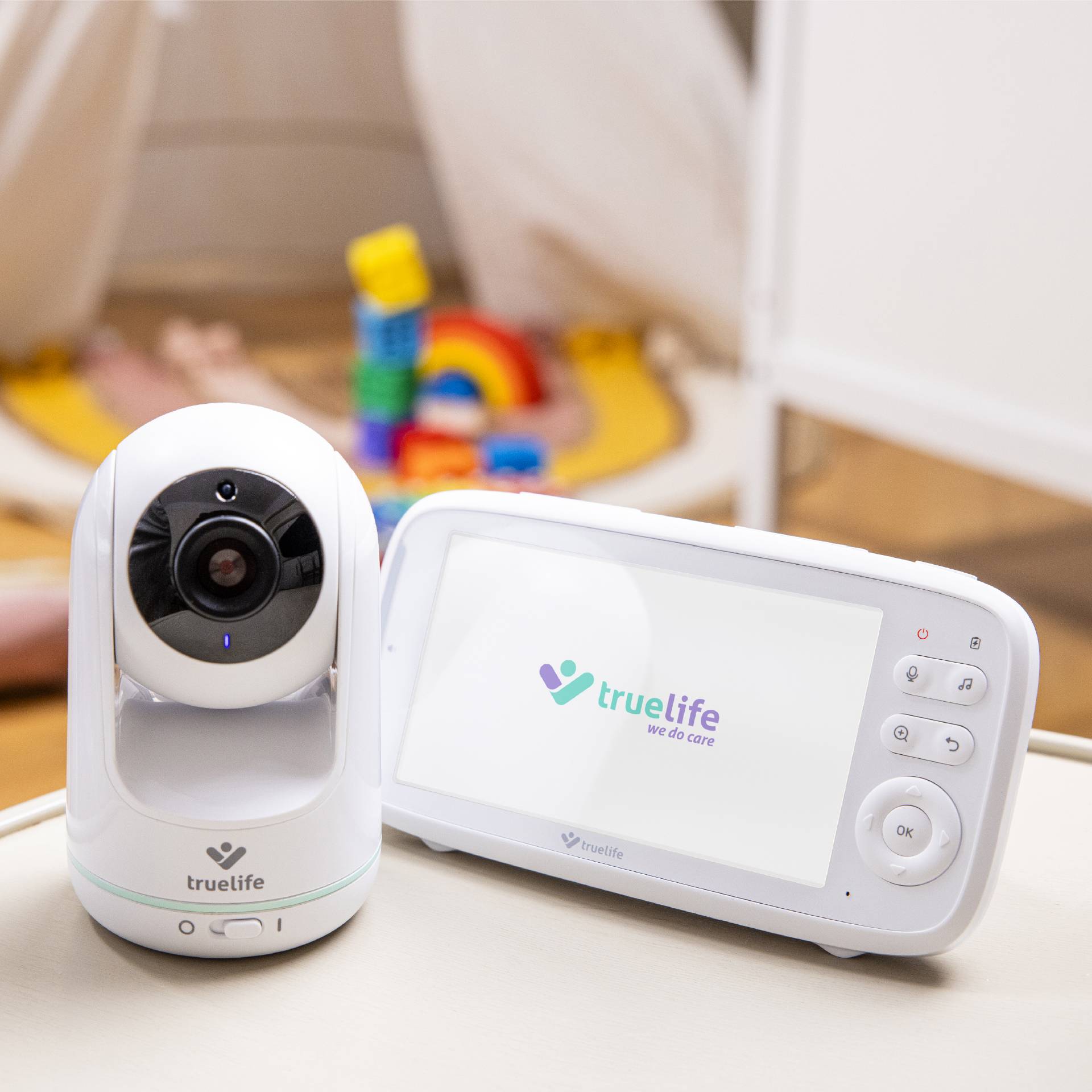 Ein Babyphone mit Kamera und Monitor zeigt ein Kind, das auf dem Boden spielt. Das Logo 'truelife - we do care' ist sichtbar.