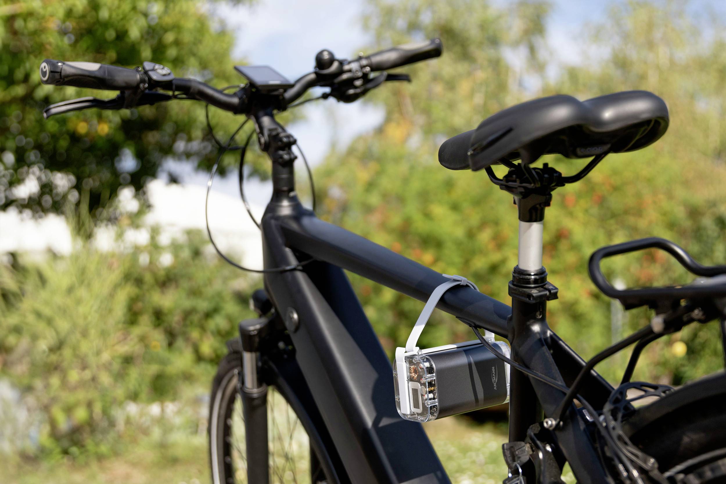 E-Bike mit befestigtem GPS-Gerät am Rahmen. Im Hintergrund Bäume und ein bewölkter Himmel. Fokus auf die Technologie des Fahrrads.