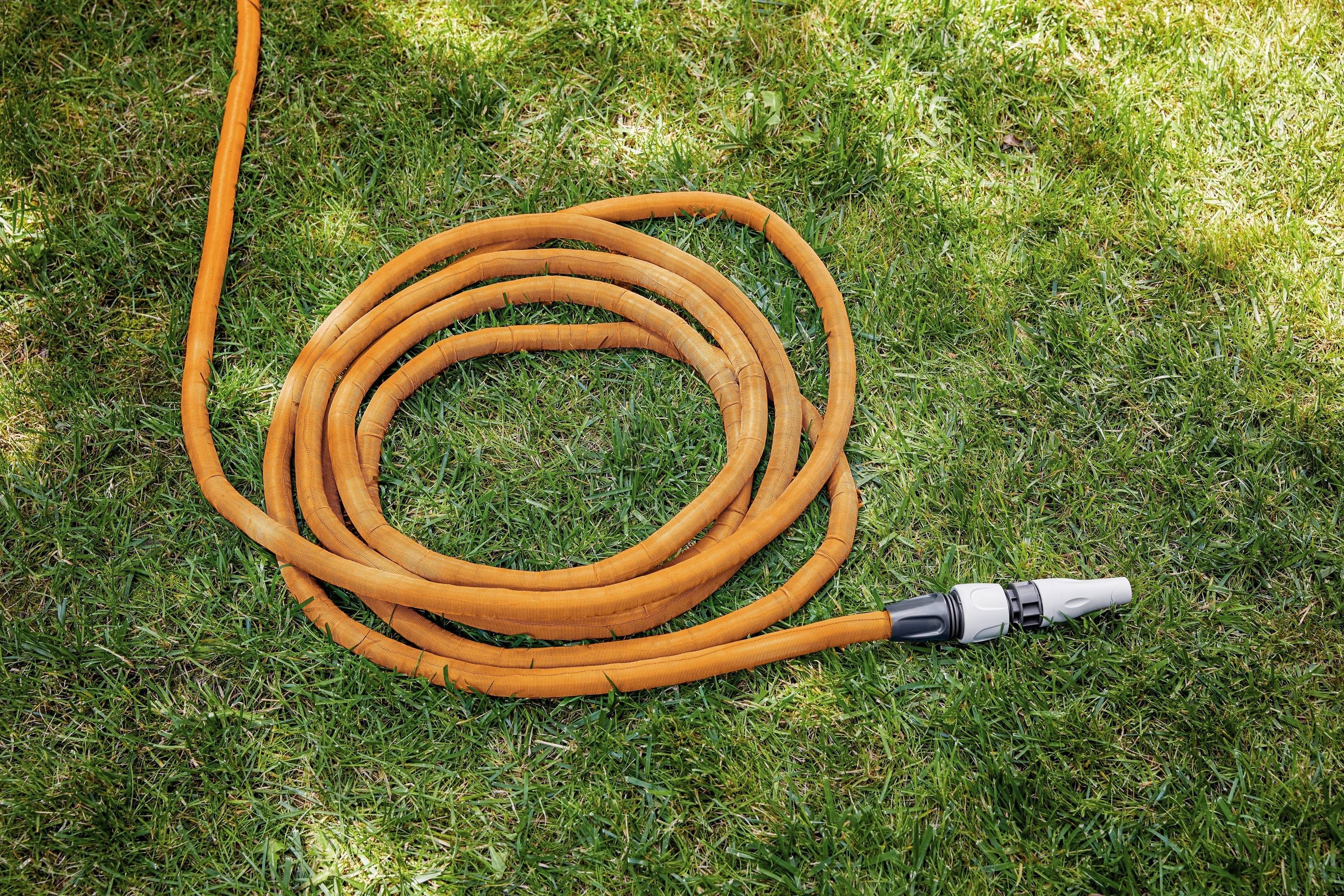 Ein orangefarbener Gartenschlauch liegt auf grünem Gras, spiralförmig zusammengerollt, mit Anschlussstück an einem Ende sichtbar.