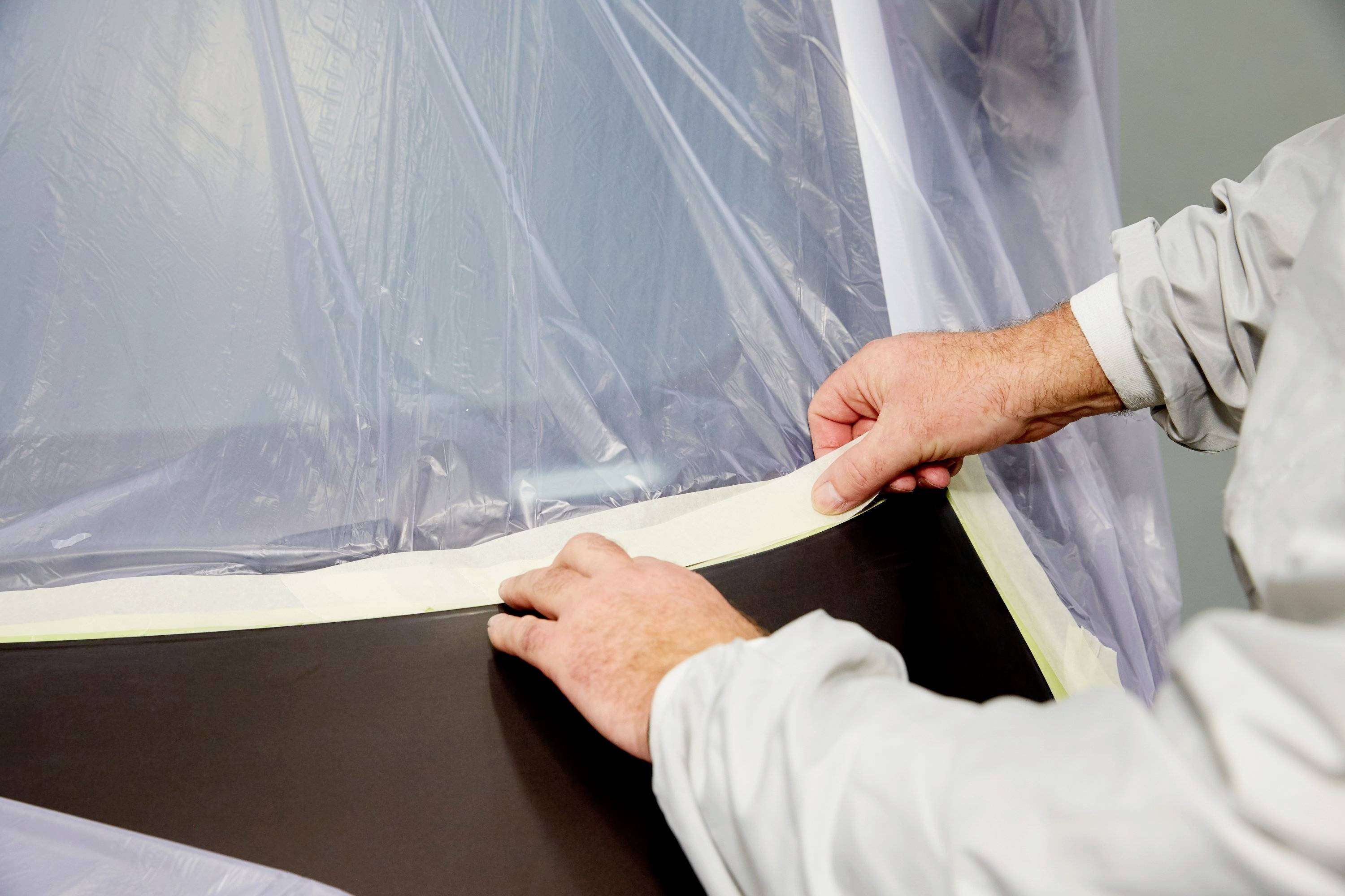 Hände eines Mannes kleben Klebeband an den Rand einer Plastikabdeckung.