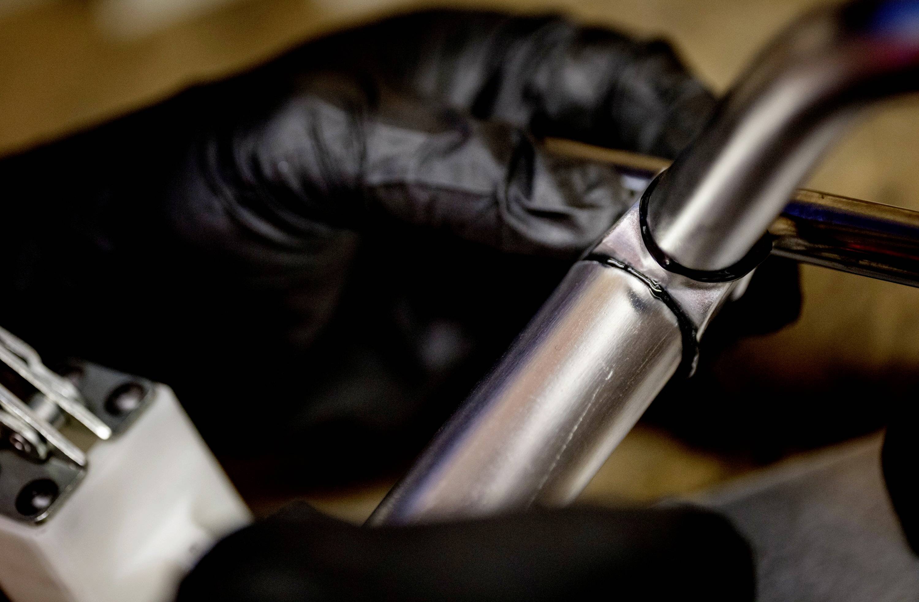 Eine Person mit schwarzen Handschuhen schweißt zwei Metallrohre zusammen, die Elektroden des Schweißgeräts sind sichtbar.