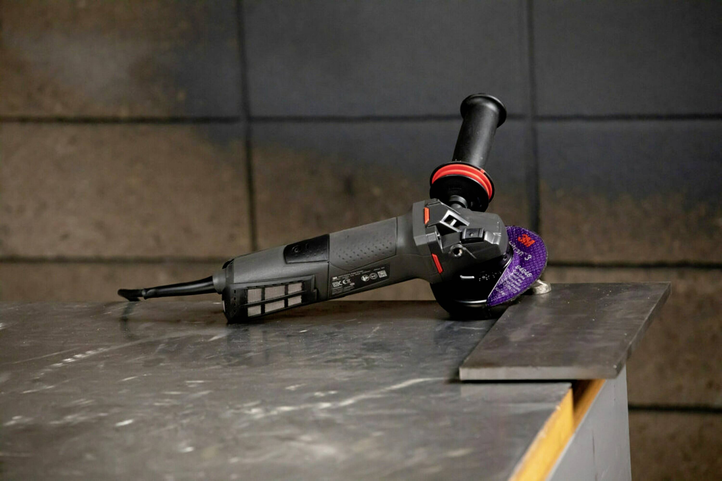 Eine Winkelschleifermaschine liegt auf einem Metalltisch, bereit zur Verwendung. Sie ist schwarz mit roten Akzenten.